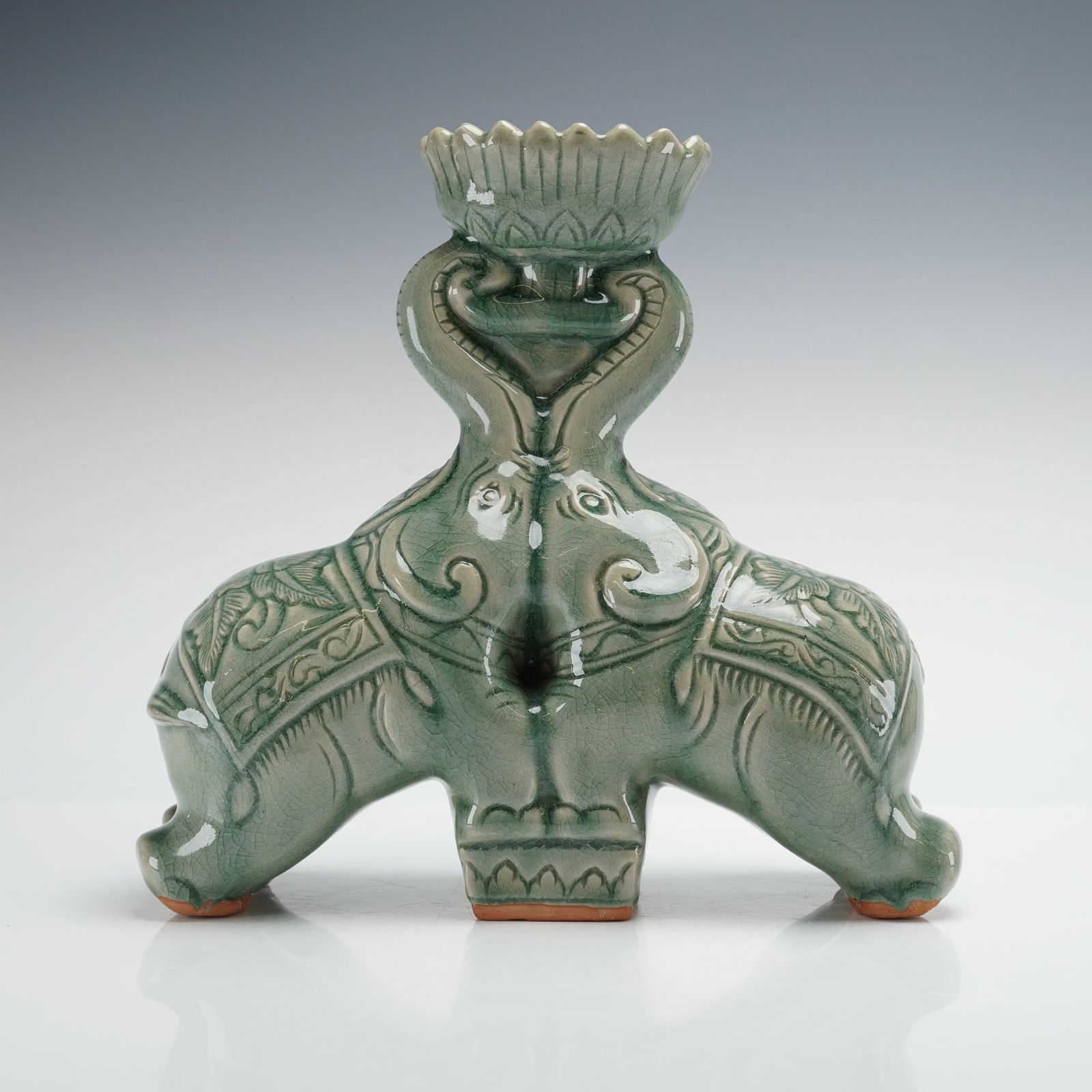 Thai Baan Celadon Glaze Elephant Figures Stand w/ Receptacle: A Baan Celadon ceramic figurine, handcrafted in Chiang Mai, Thailand. This piece is designed as a decorative stand or candleholder, featuring two elephants standing back-to-back with their intertwinin