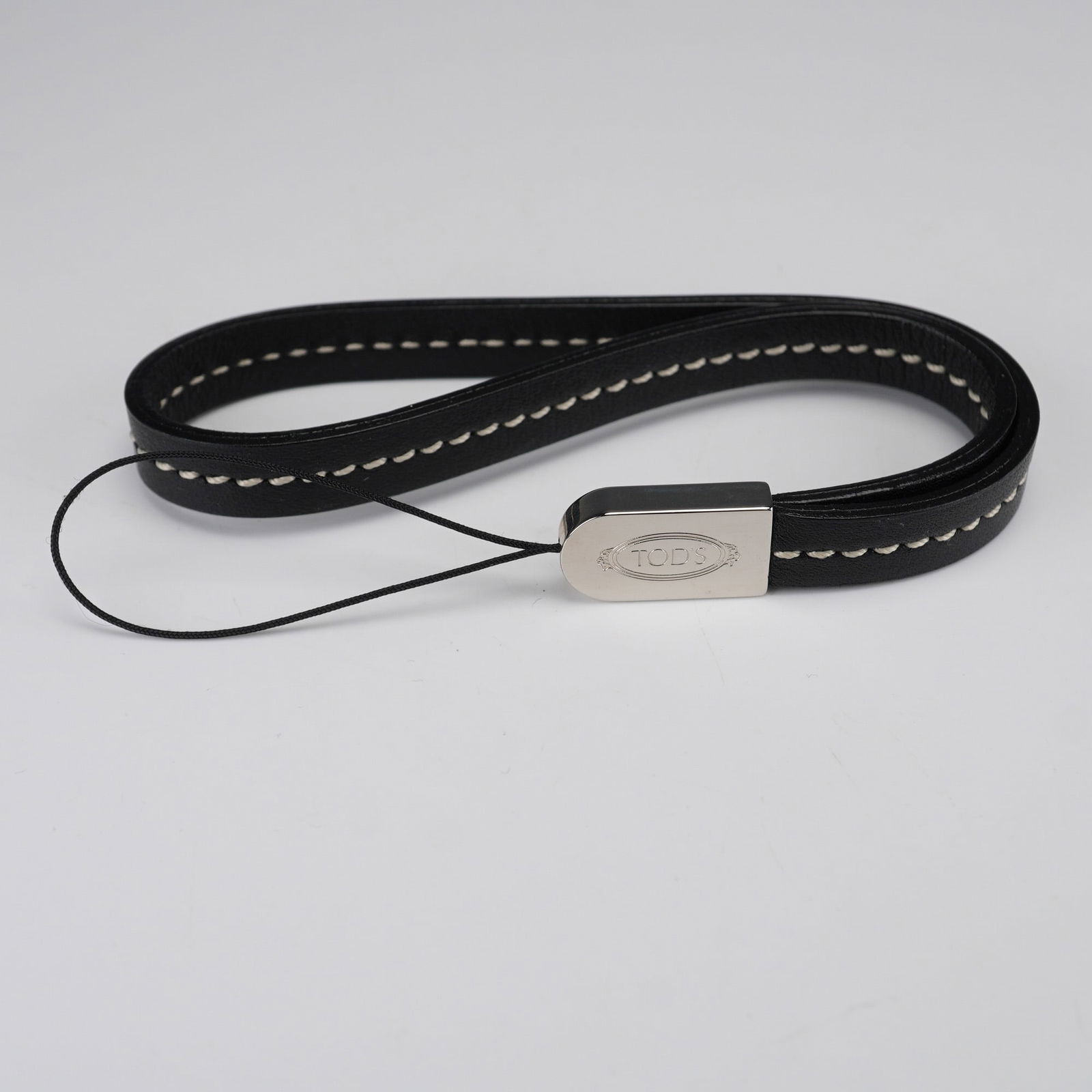 Tod's Black Leather Device Lanyard with White Contrast Stitching: A Tod's black leather device lanyard, characterized by its prominent white contrast stitching. It features a silver-tone metal fitting, prominently displaying the 'TOD'S' logo, from which a thin