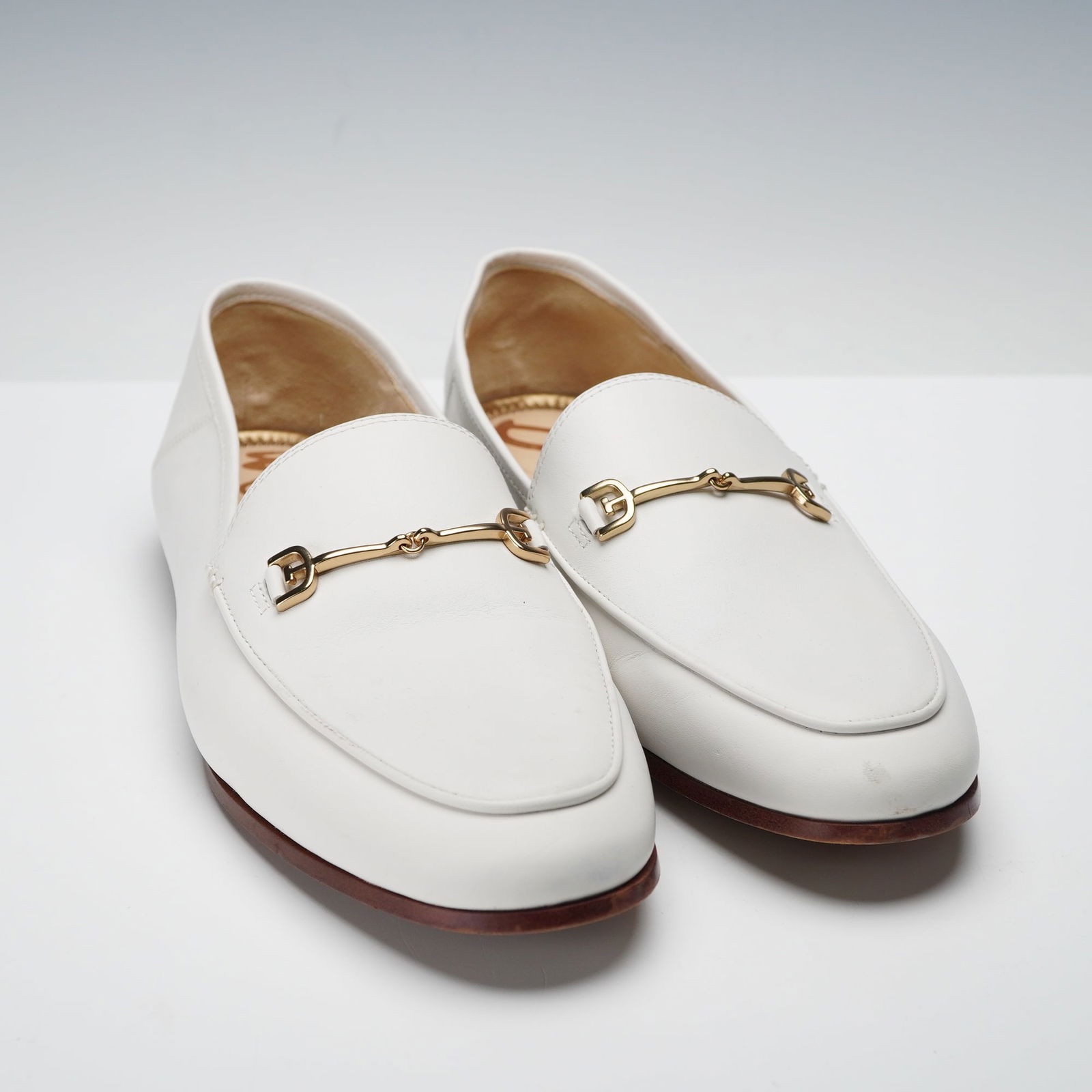 A Pair of Sam Edelman Loraine Bit White Leather Loafers: A pair of Sam Edelman Loraine Bit Loafers in white leather, styled in a classic slip on design with stitched moc toes and signature gold tone snaffle hardware across the vamps. The flat brown soles