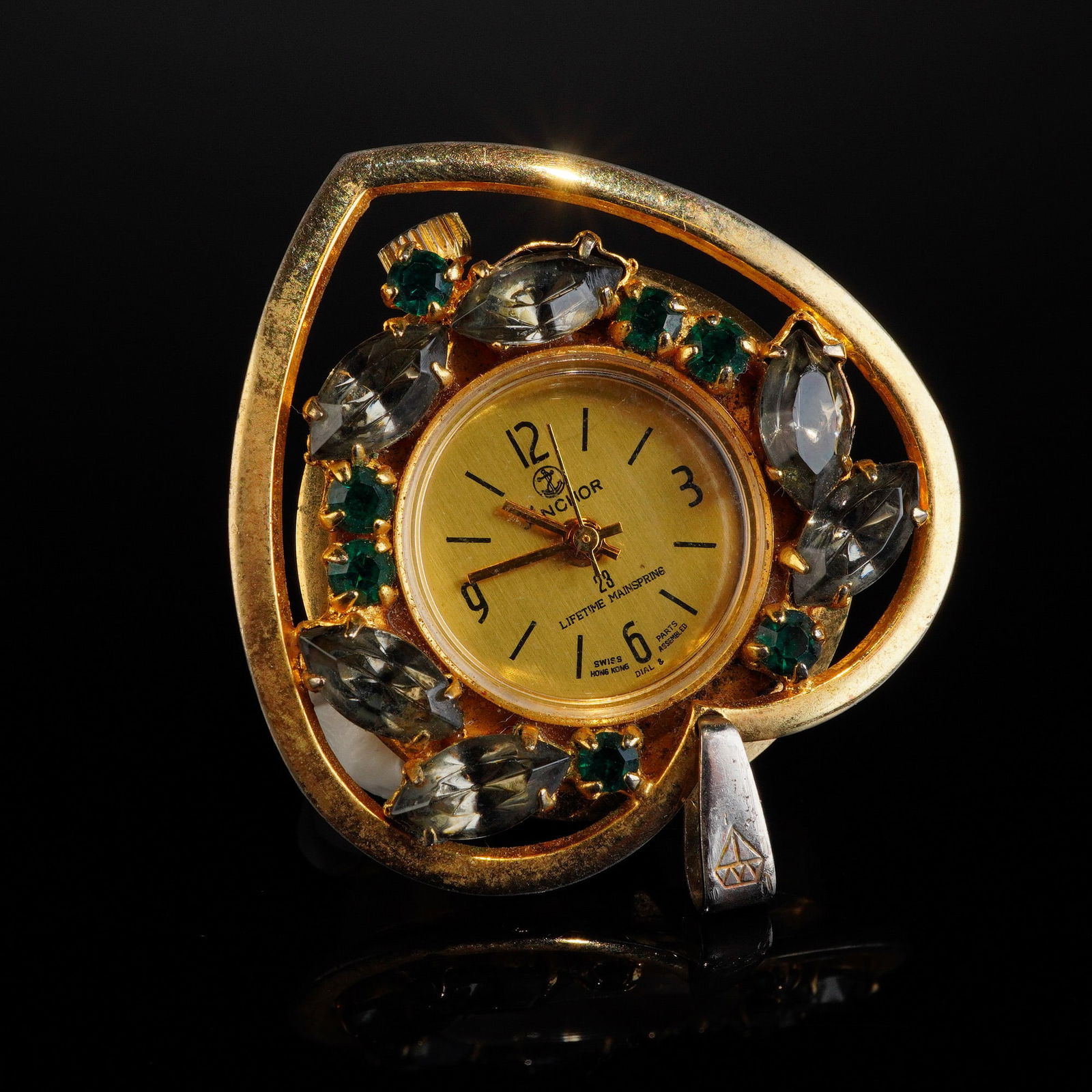 Vintage Anchor 23 Jewel Gem Inlaid Gold Toned Pendant Watch: A single vintage convertible pendant watch featuring a gold-toned setting shaped like a stylized heart or teardrop. The setting is inlaid with large, faceted smoky gray rhinestones and smaller