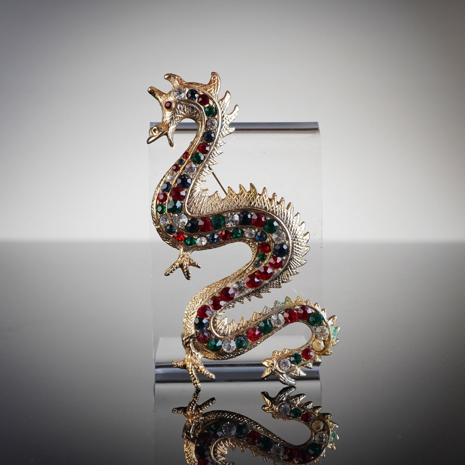 Rhinestone Dragon Brooch: The object is a single figural costume jewelry brooch, styled as a serpentine Eastern-style dragon. The piece is constructed from gold tone base metal, utilizing a cast technique. The body of the drag