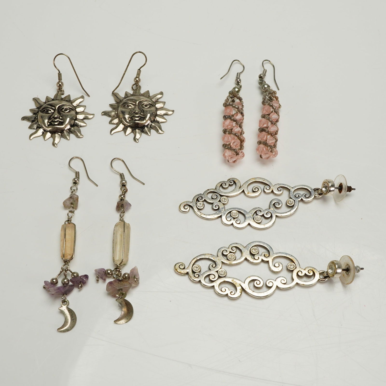 Four Pairs of Silver Tone Celestial and Fashion Dangle Earrings: A collection of four pairs of costume or fashion earrings constructed primarily from silver-toned base metal. The collection includes four distinct styles. The first pair features large sun face dangl