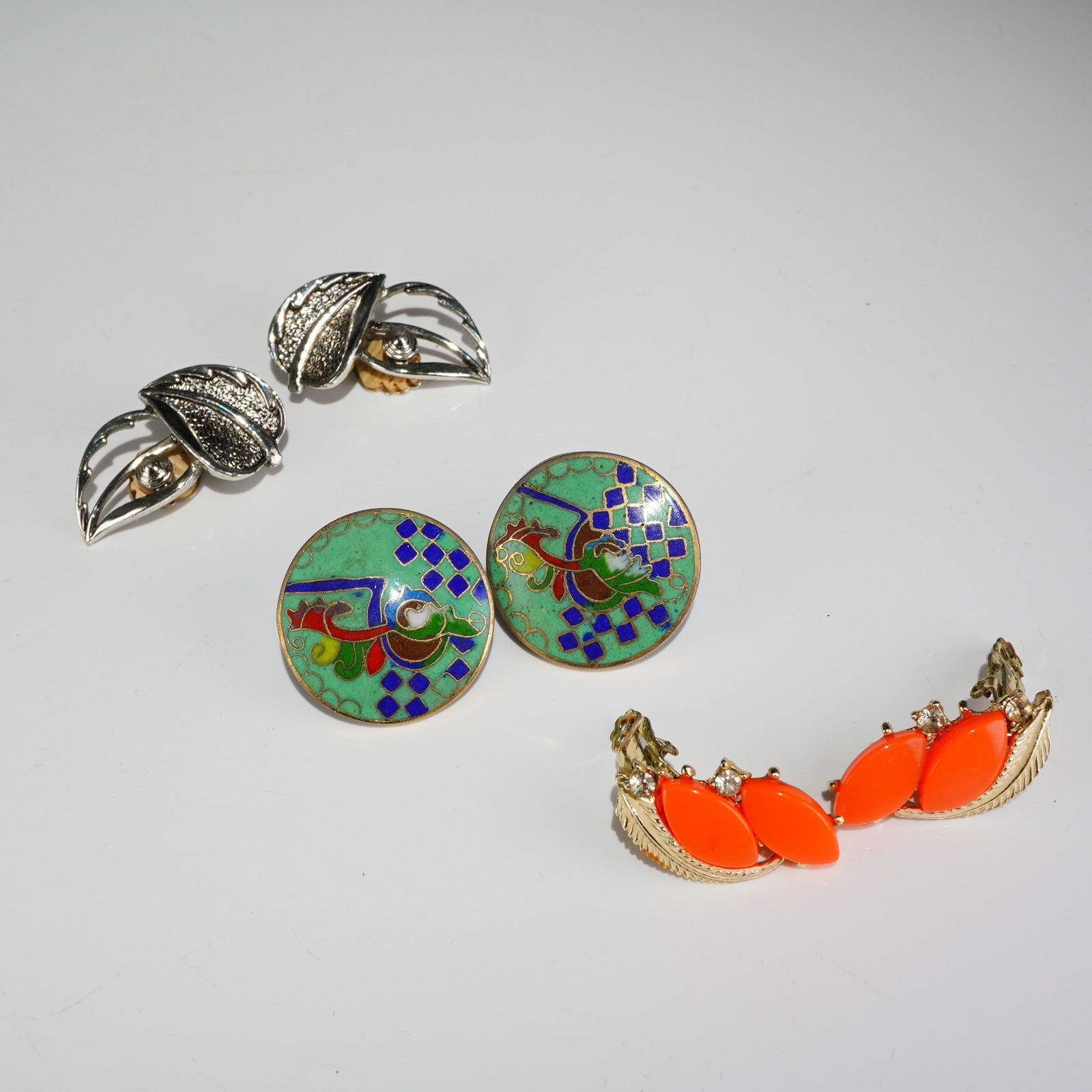 3 Pairs Vintage Clip-On Earrings incl. Sarah Cov & Cloisonne: A collection of three pairs of vintage costume clip-on earrings. The first pair consists of silver-tone clip-back earrings designed in a layered leaf motif. The finding is clearly marked SARAH COV and