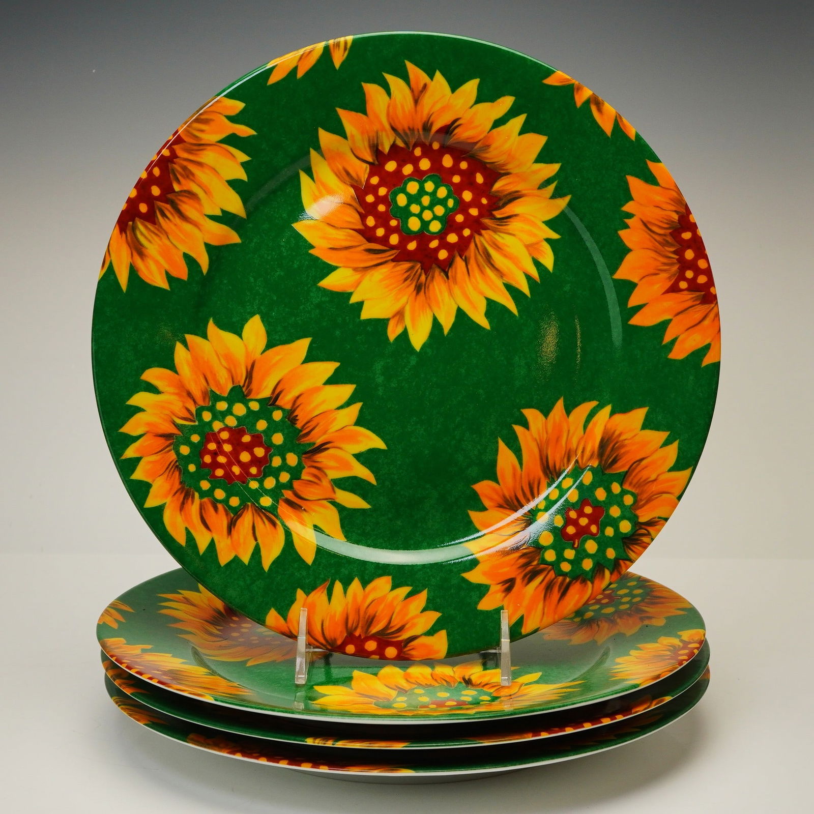 4pc Laure Japy Limoges France Porcelain Plates, Tournesol Green: Each plate features a vibrant sunflower motif in shades of yellow, orange, and red set against a mottled dark green background. The contemporary design is applied to a classic circular form. The