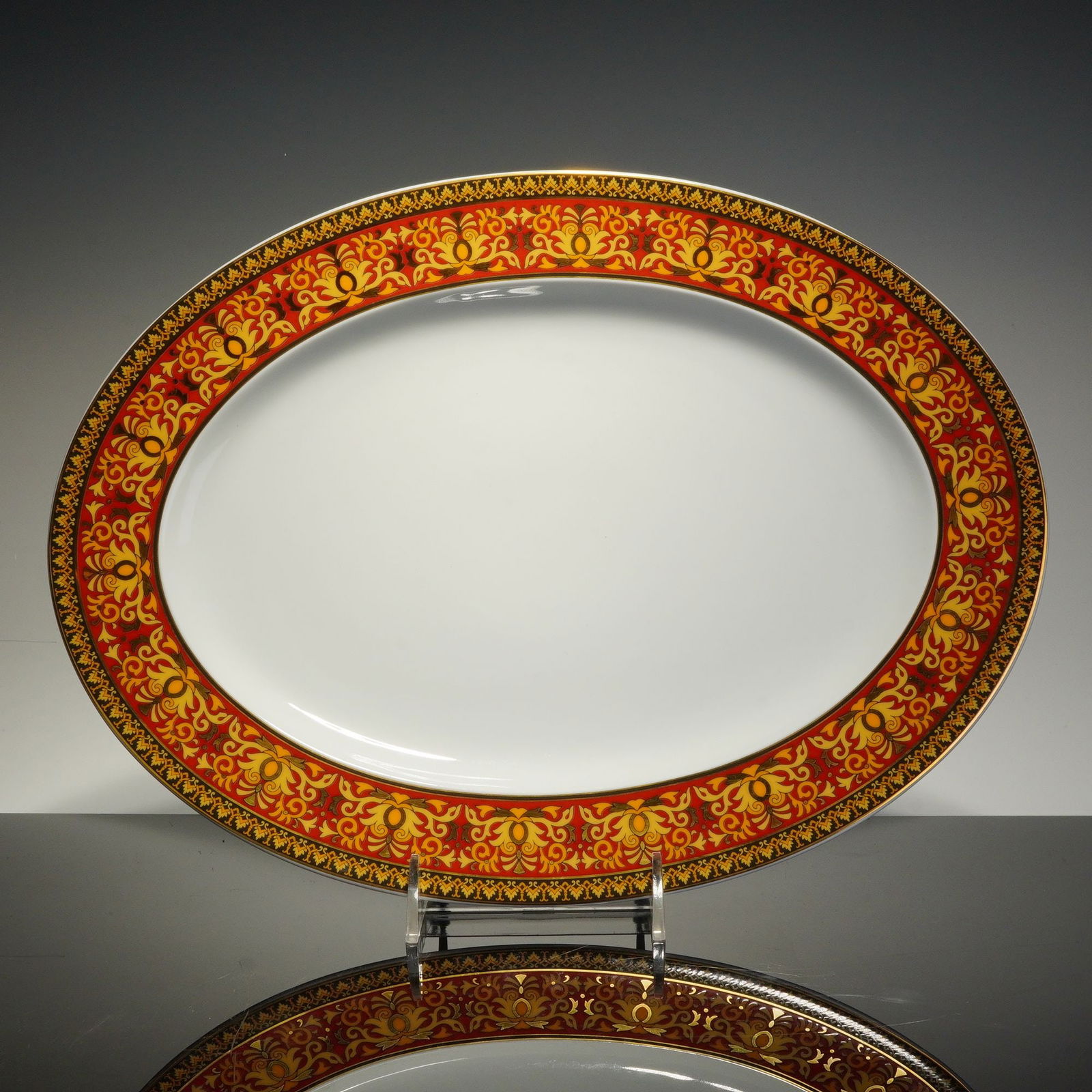 Rosenthal Versace Medusa Red Porcelain Oval Serving Platter: A Rosenthal for Versace porcelain oval serving platter from the Medusa Red collection. The piece features a white ground with an ornate decorative border. The wide rim is decorated with a vibrant red