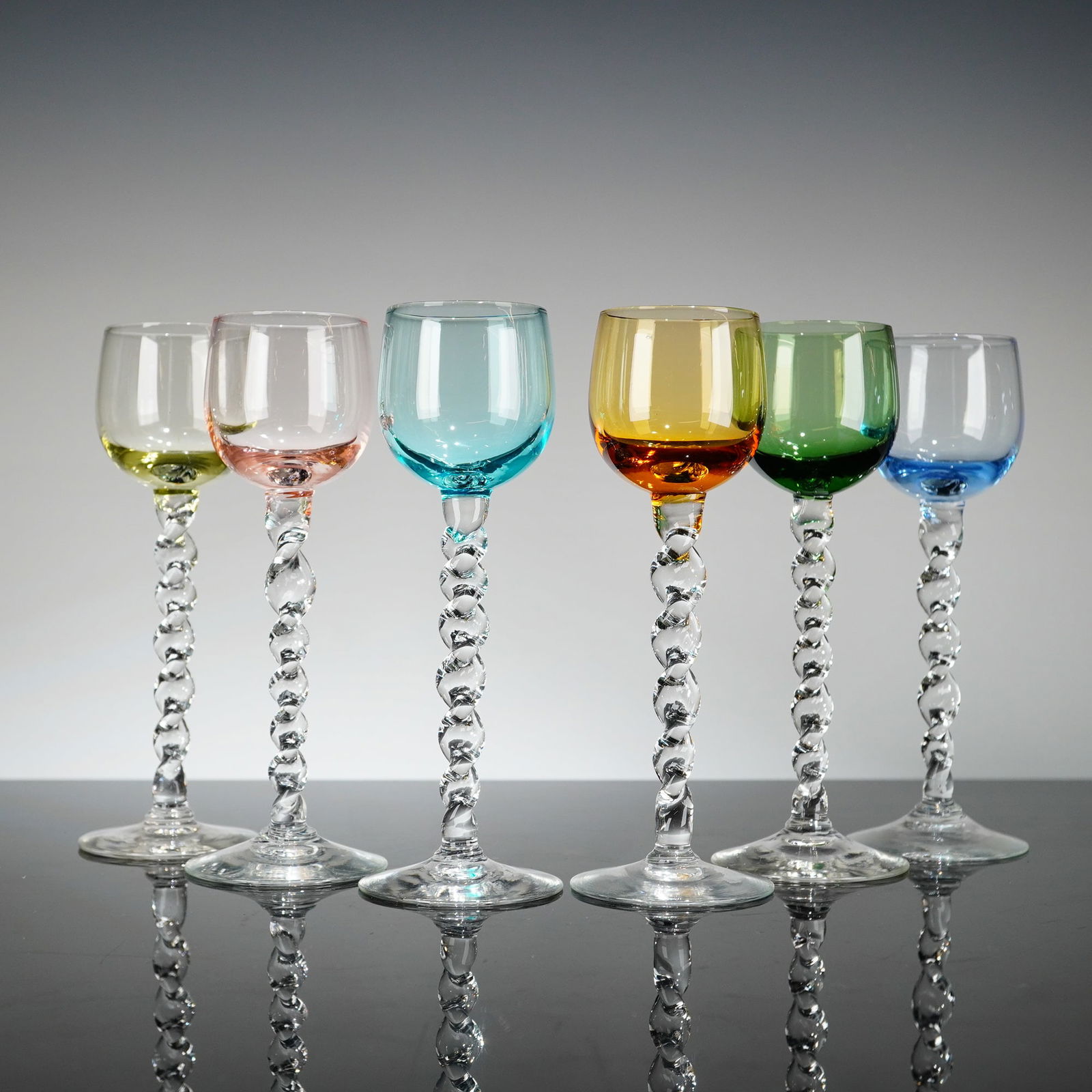 6pc Colored Stemware Cordial Glasses with Barley-Twist Stems: These six stemware cordial glasses features rounded, colored bowls supported by clear glass barley-twist stems. Each ends in a wide, circular clear glass base with a slightly recessed center. Dimensio