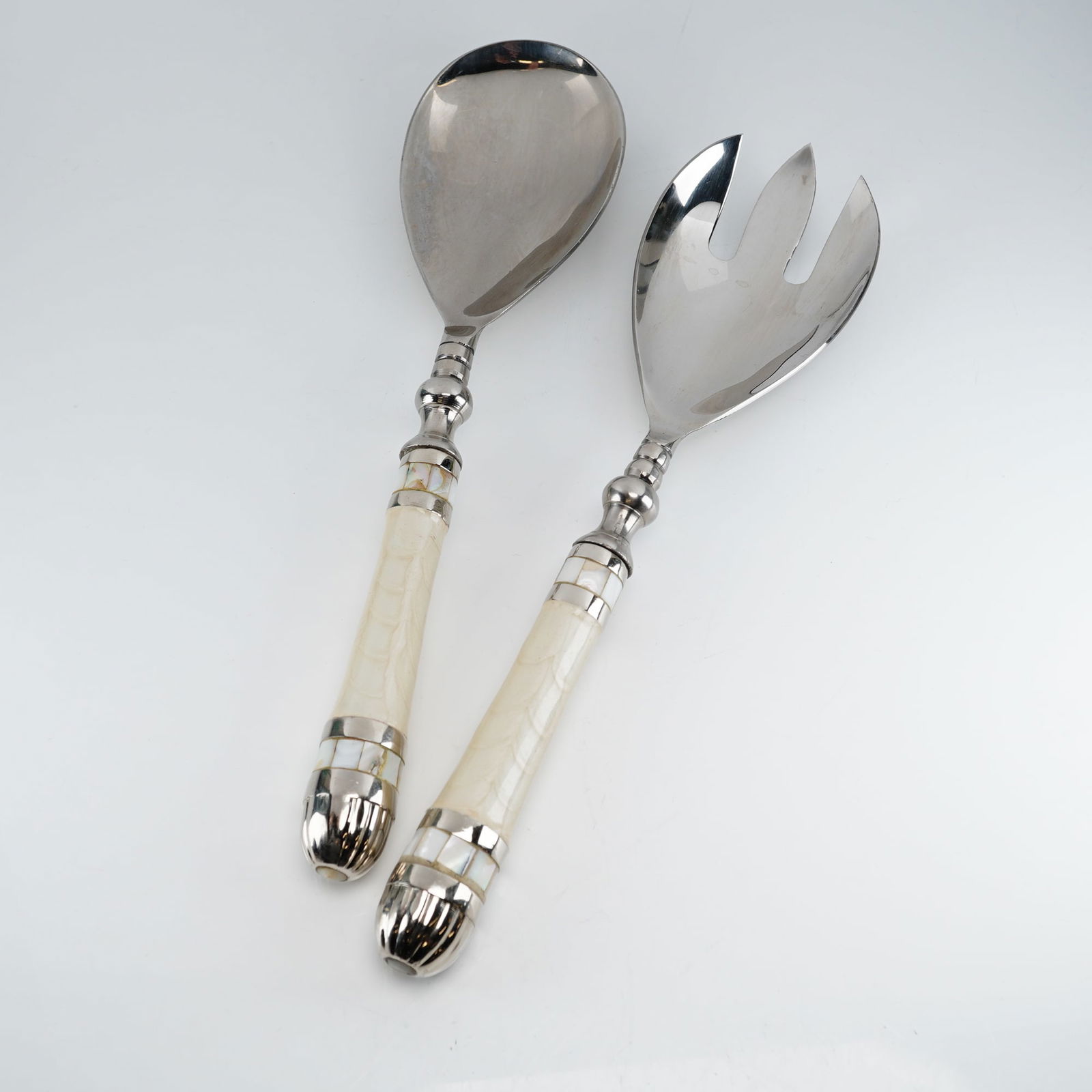 2pc Julia Knight Mother of Pearl Serving Utensils: The set consists of one serving spoon and one three-tined serving fork. Each piece features polished silver-toned metal heads and ornate handles. The handles are designed with a central cream-colored