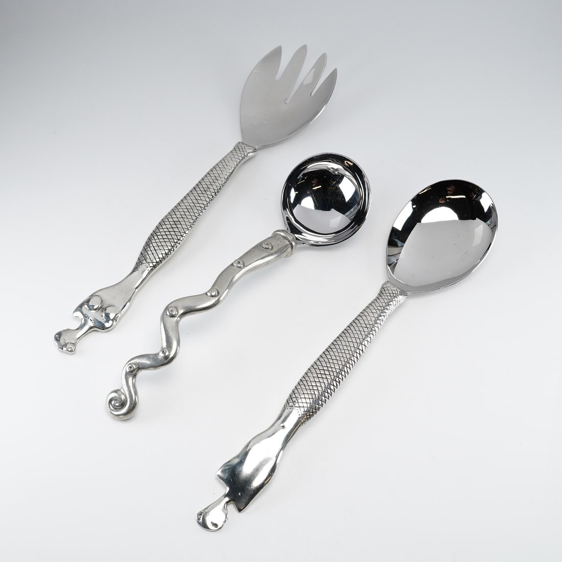 3pc Carrol Boyes Silverplated Serving Spoons and Fork: This 3pc set consist of a large serving spoon, a large serving fork, and a small ladle. The pieces are designed with stylized organic and figural motifs. The handles of the fork and spoon feature a