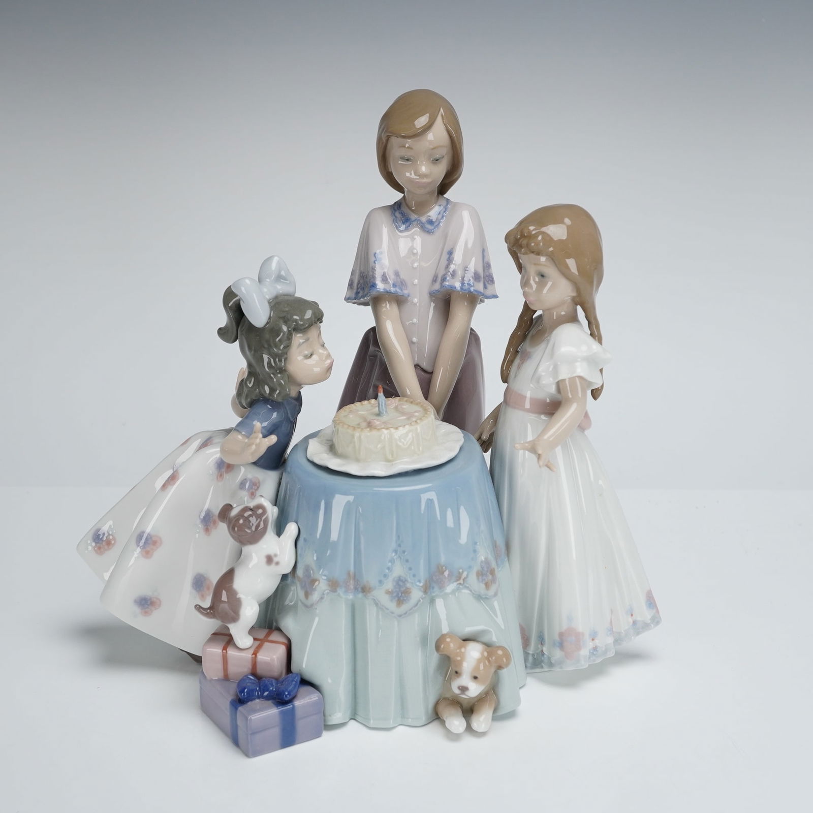 Lladro Hand-Painted Porcelain Making a Wish Group Figurine 1005910: A Lladro porcelain figurine group titled Making A Wish, Item #1005910. The single glazed porcelain figurine depicts a birthday scene featuring three young girls gathered around a draped light blue