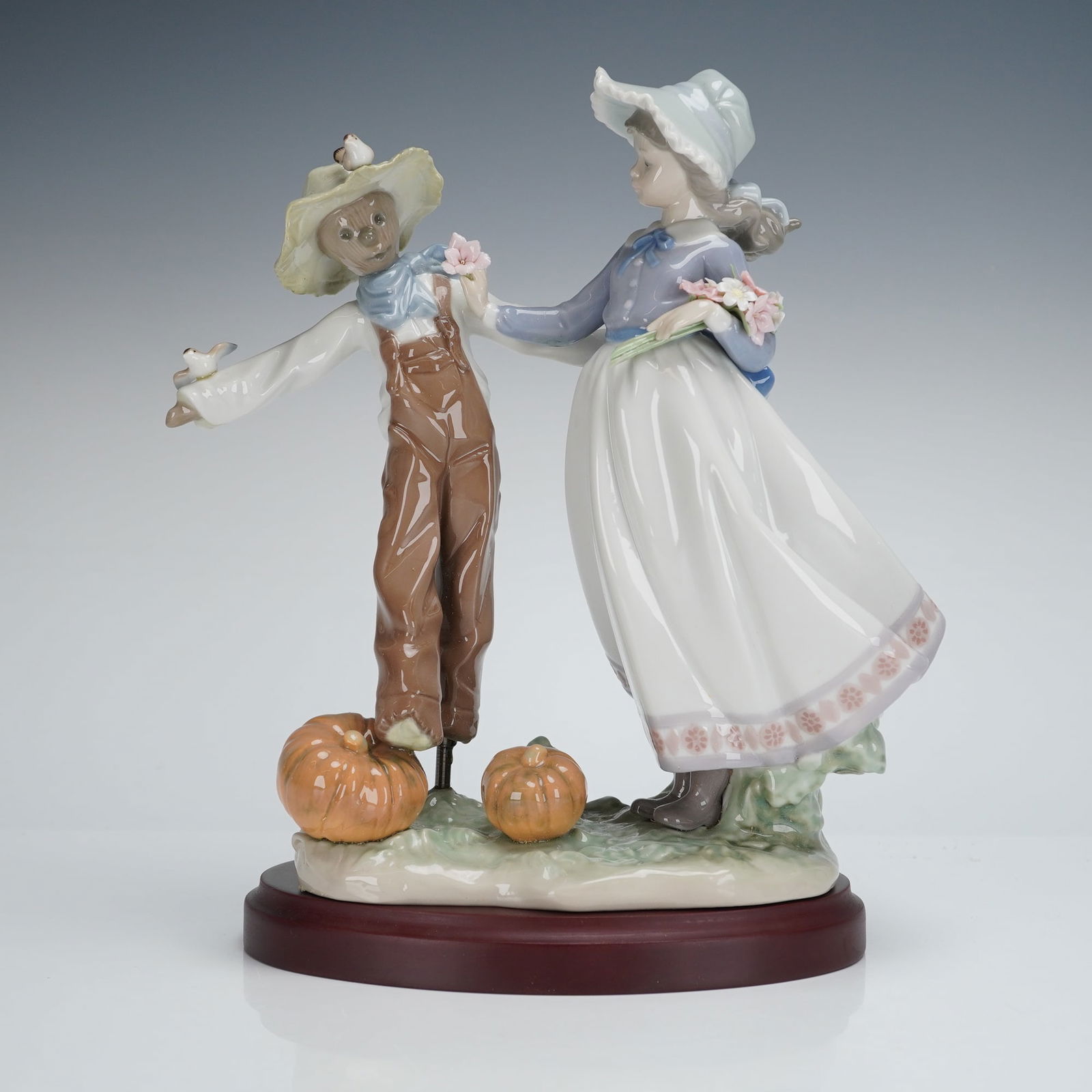 Lladro Scarecrow and the Lady Figurine 5385: A Lladro Porcelain Figurine titled Scarecrow and the Lady, model number 5385. This glazed porcelain figural group depicts a young girl in a white skirt, lavender top, and bonnet interacting with a