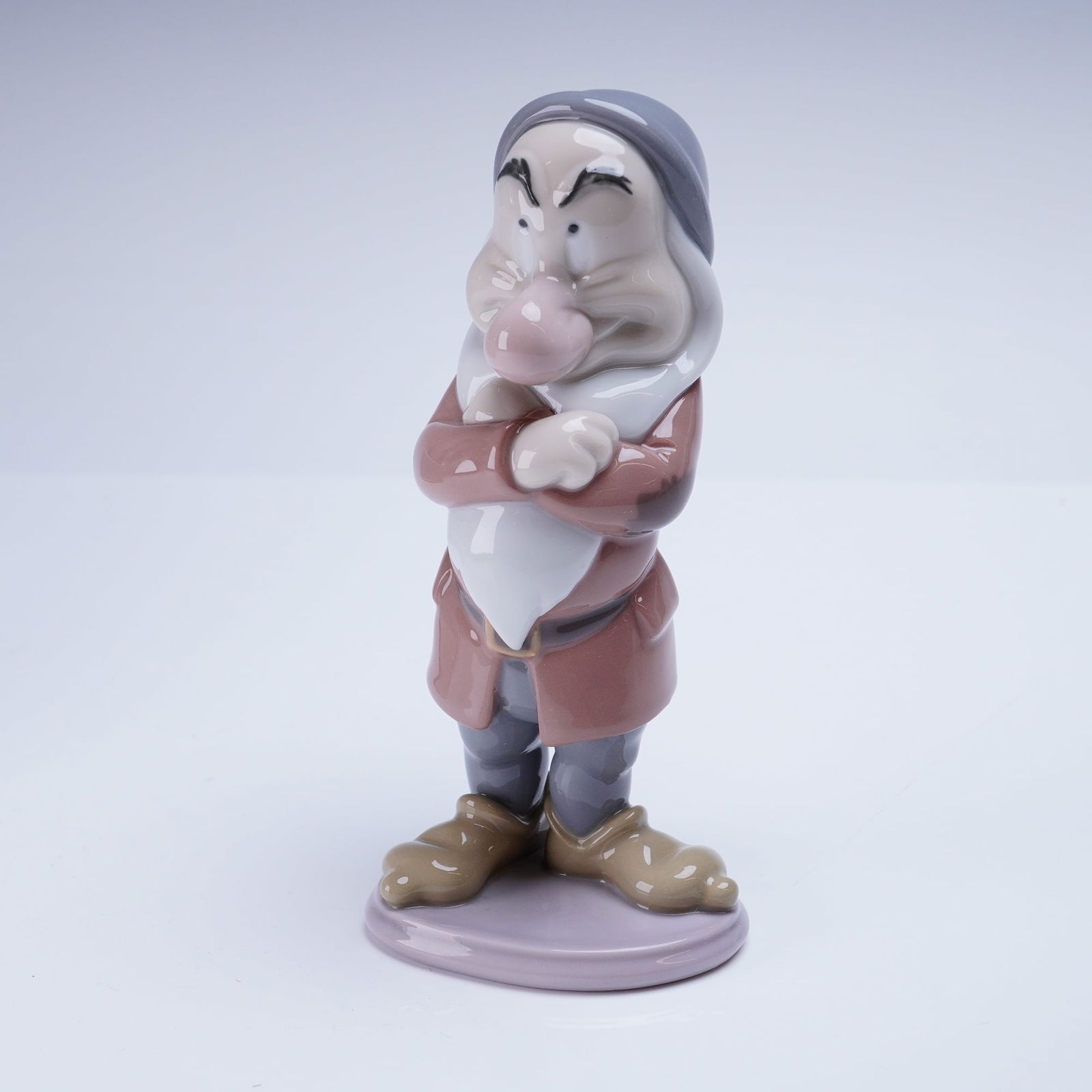 Lladro Disney Dwarf Figurine Grumpy 1007538: A single glazed porcelain figurine by Lladro, model number 01007538, depicting the Disney character Grumpy Dwarf from Snow White and the Seven Dwarfs. This Lladro Porcelain Figurine is executed in a