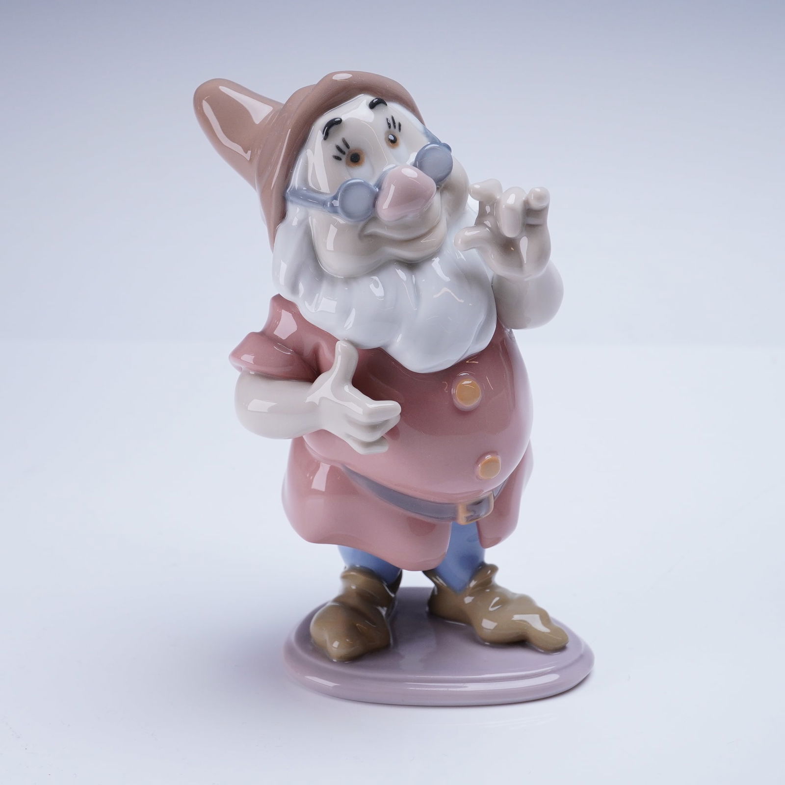 Lladro Disney Dwarf Figurine, Doc 1007533: A glazed porcelain figurine depicting the Disney character Doc, one of the Seven Dwarfs, identified by the Lladro model number 1007533. The figurine is rendered in a highly polished glaze, featuring