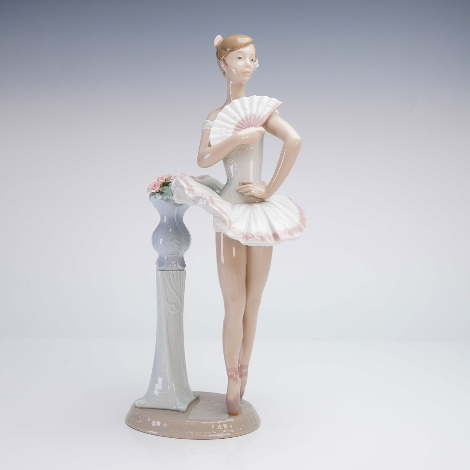 Lladro Ballerina Porcelain Figurine, En Pointe 6371: This Lladro En Pointe sculpture, model number 6371, depicts a ballerina in a white and pink tutu holding an open fan. The figure is positioned leaning against a slender pedestal topped with hand-model