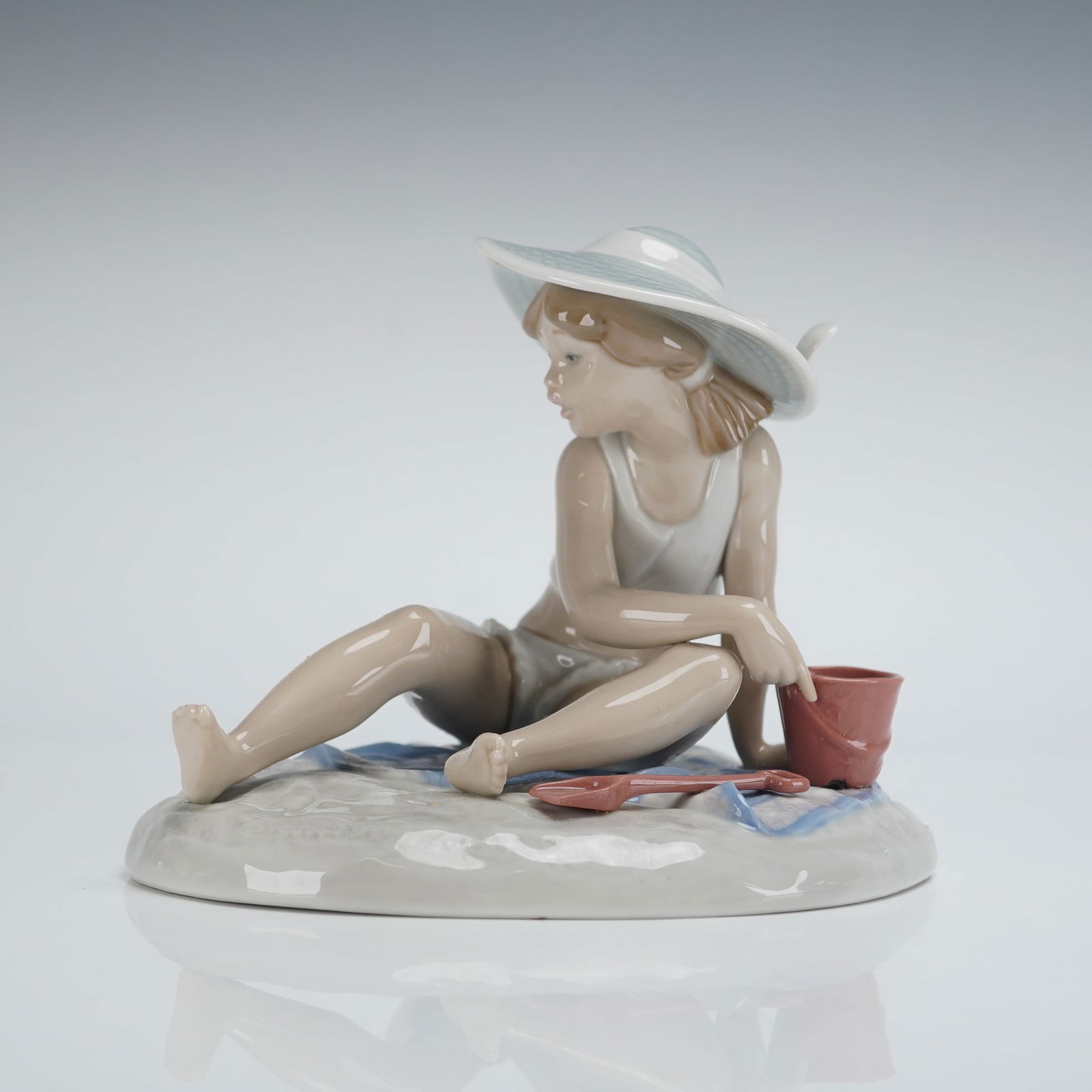 Lladro Hand-Painted Porcelain Sandcastles Figurine by Regino Torrijos 5488: A single Lladro porcelain figurine designed by Regino Torrijos, model 5488, titled Sandcastles. The piece depicts a young girl seated on a simulated beach base, executed in the sentimental