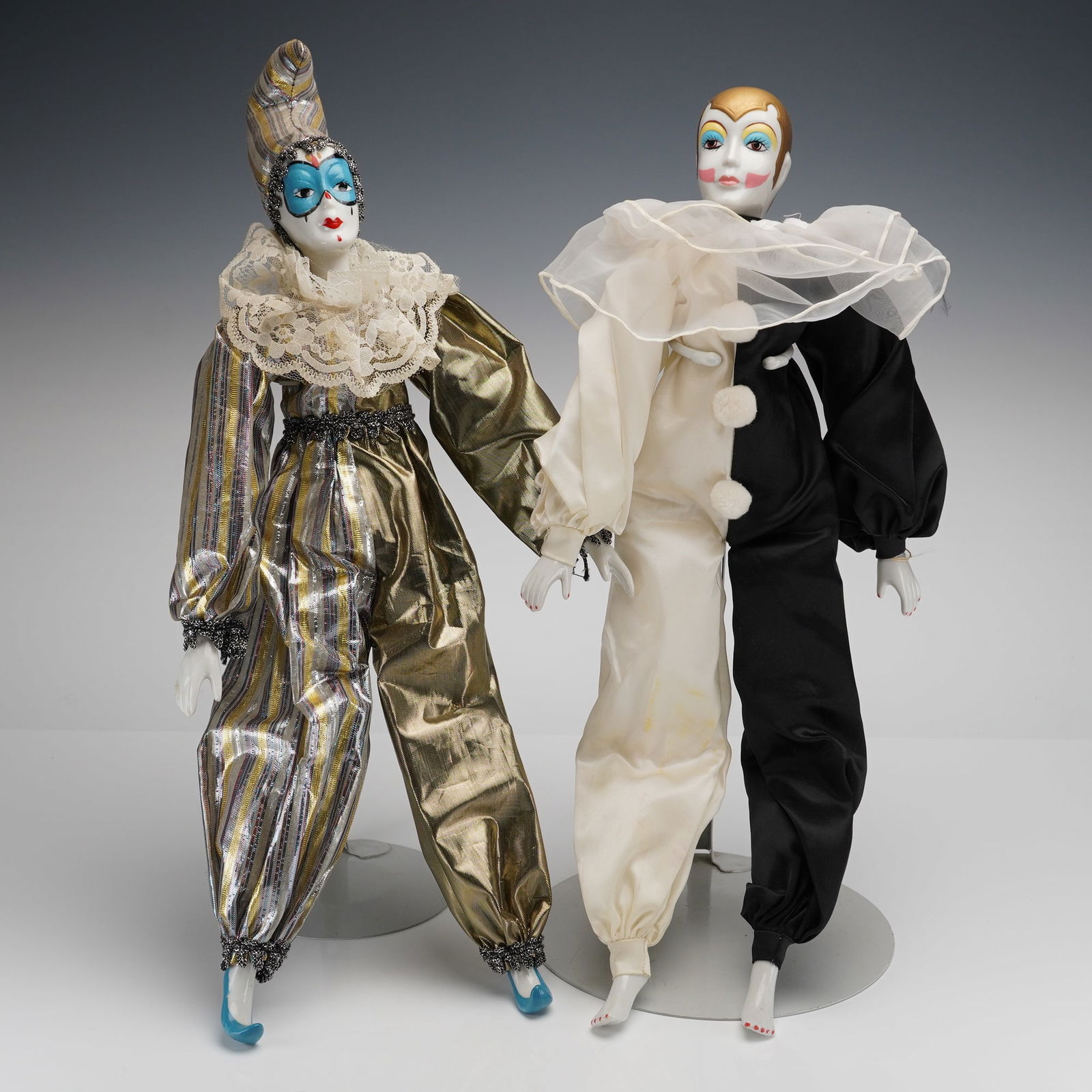 A Pair of Russ Berrie Porcelain Harlequin Jester Dolls: A pair of collector's dolls, styled as Harlequins, featuring porcelain heads, hands, and feet, with soft stuffed bodies. The dolls are attributed to Russ Berrie, based on a visible fabric tag on the r