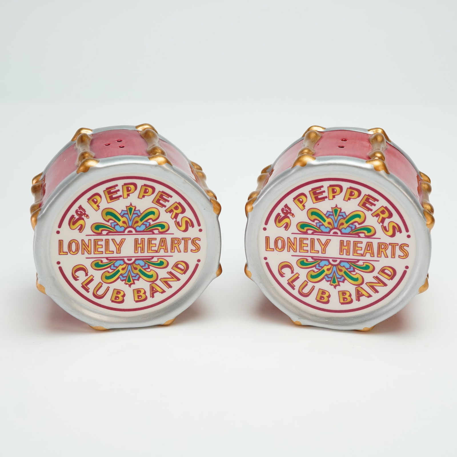 Vandor Dist. Pair of Beatles Sgt Peppers Ceramic Drum Shakers: A pair of Vandor ceramic novelty salt and pepper shakers designed in the form of bass drums, inspired by The Beatles' Sgt. Pepper's Lonely Hearts Club Band album cover. Each shaker features a red-glaz