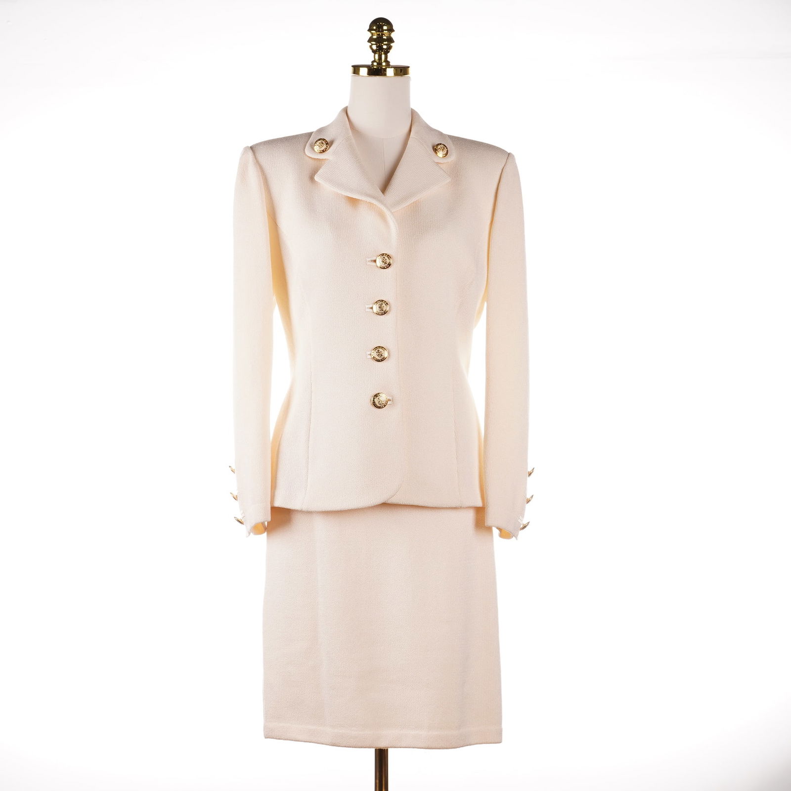 2pc St. John Basics Off-White Wool Knit Blazer & Matching Skirt Suit: A St. John Basics two-piece ensemble including an off-white wool knit blazer and matching skirt. The blazer features a notched lapel accented with decorative gold-tone buttons embossed with the brand