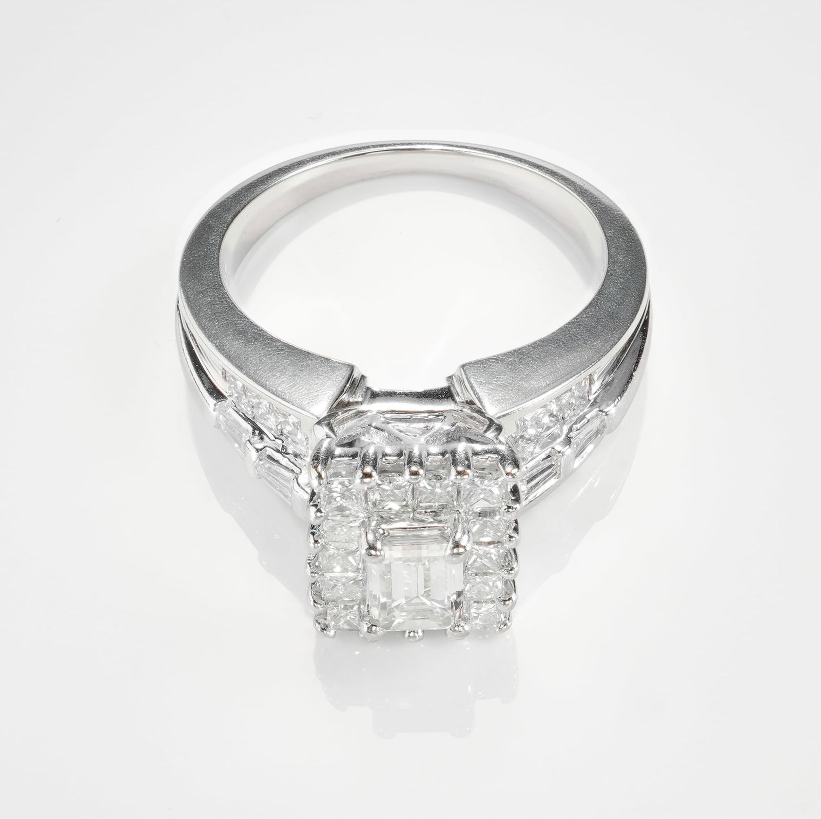18K White Gold 1.00ctw Diamond Ring: This refined ring features an emerald cut diamond at the center, framed by a halo of square cut diamonds that echo its crisp geometry. The shoulders are further accented with tapered baguette