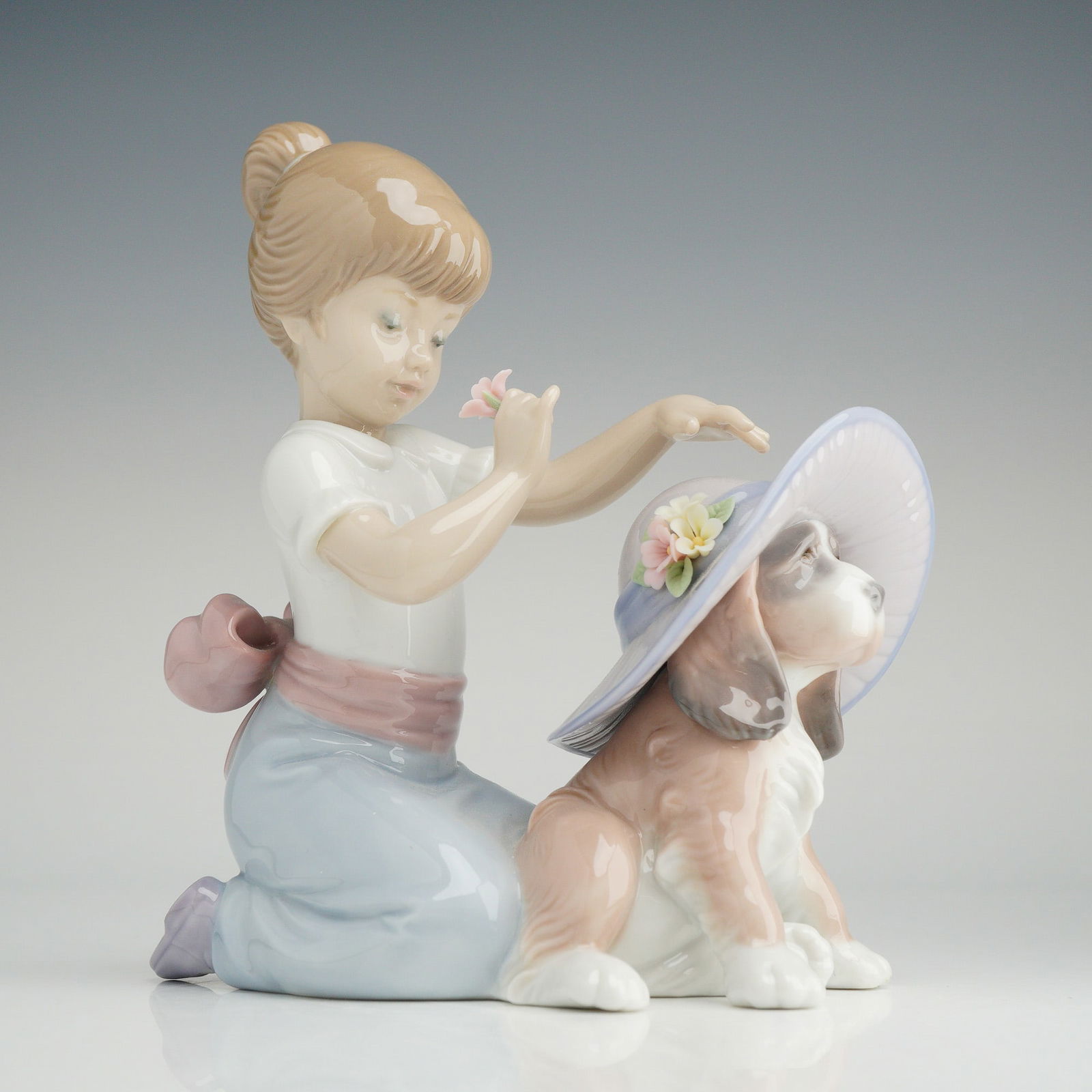 An Elegant Touch Lladro Porcelain Figurine Item 1006862: Lladro porcelain figurine titled An Elegant Touch, model number 01006862. The glazed porcelain sculpture depicts a young girl with blonde hair in a ponytail kneeling to place a lavender wide-brimmed h