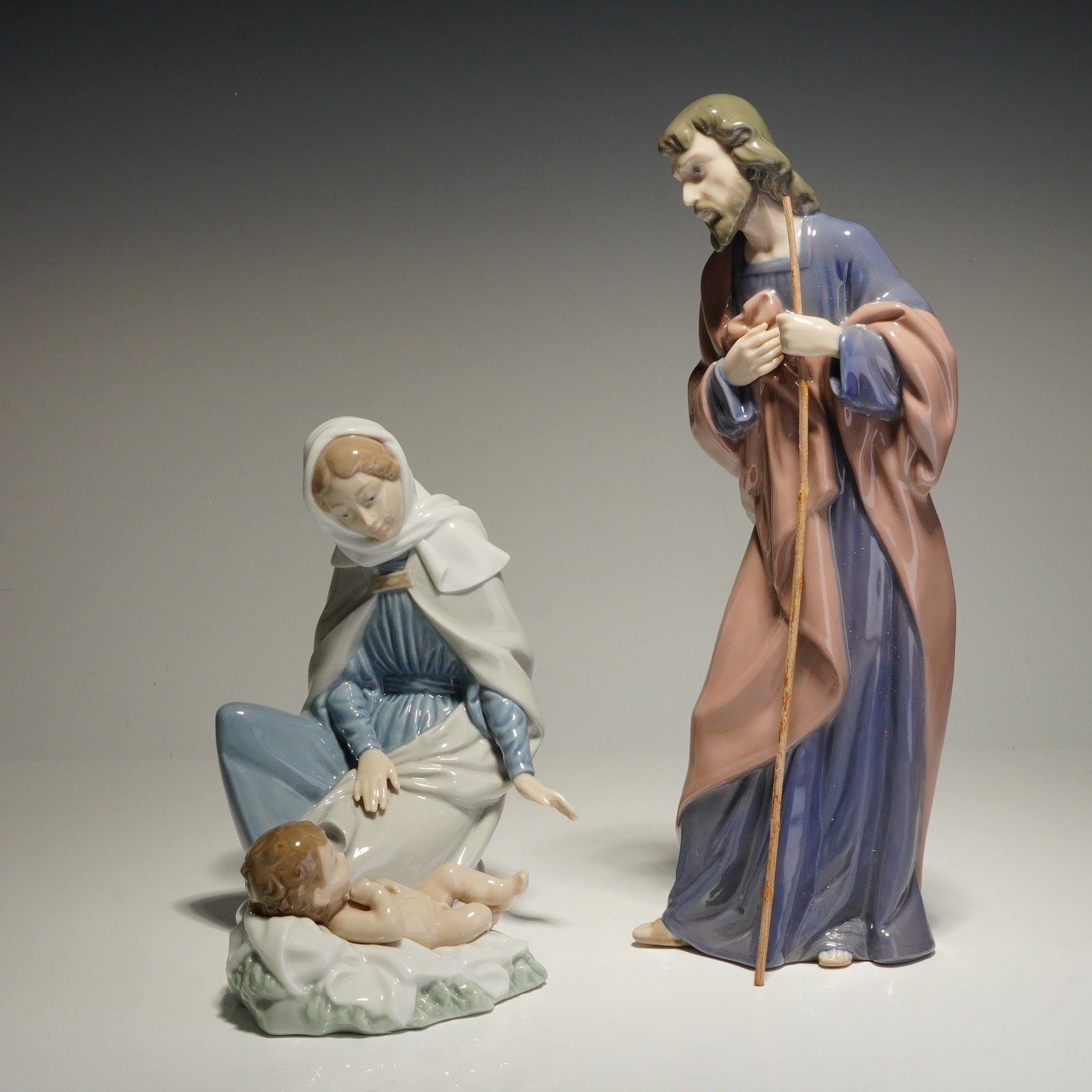 Set of Three Nao by Lladro Nativity Porcelain Figurines: The collection includes Saint Joseph (model 0306), Mary (model 0307), and the infant Jesus (model 0313). Each piece is finished in a soft pastel color palette. Saint Joseph is depicted standing with
