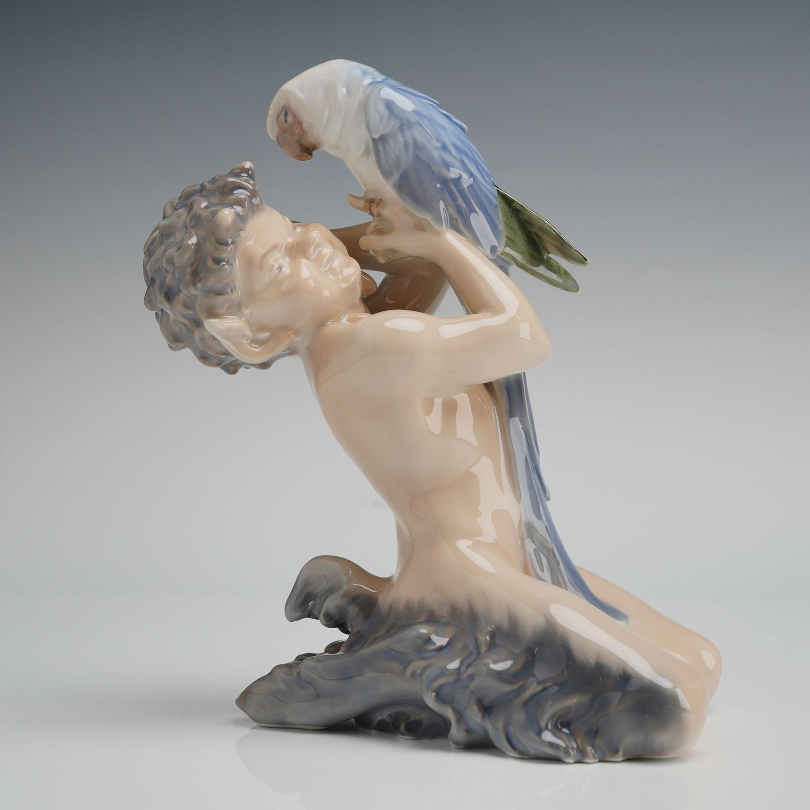 Royal Copenhagen Porcelain Figurine, Faun and Parrot 752: A Royal Copenhagen glazed porcelain figurine, model number 752, depicting a kneeling faun and parrot. The figure features a faun with cloven hooves and pointed ears holding a large parrot, designed