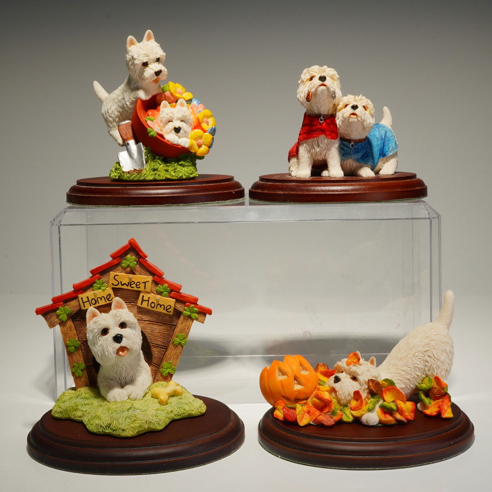 4pc Sherratt & Simpson, Peakdale West Highland Terrier Figurines with Bases: A collection of decorative figurines crafted from hand-painted composite resin. Each piece is mounted on a stepped, dark wood-tone circular base with a green felted underside. The collection features