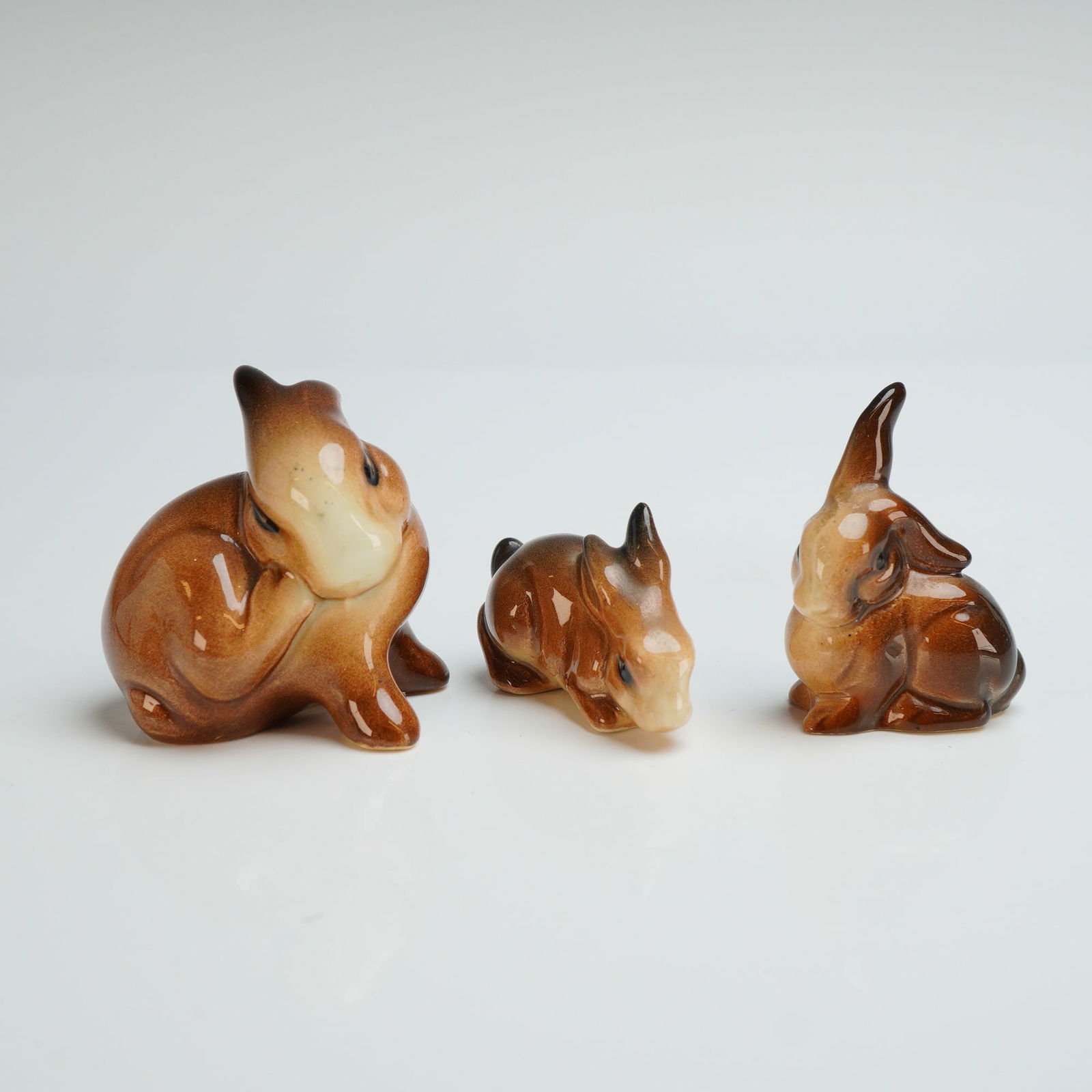 3pc Beswick Ceramic Rabbit Figurines: Finished in a high-gloss brown and tan glaze with stylized naturalistic features. The collection includes figurines in various poses, including alert, scratching, and crouching. The items are