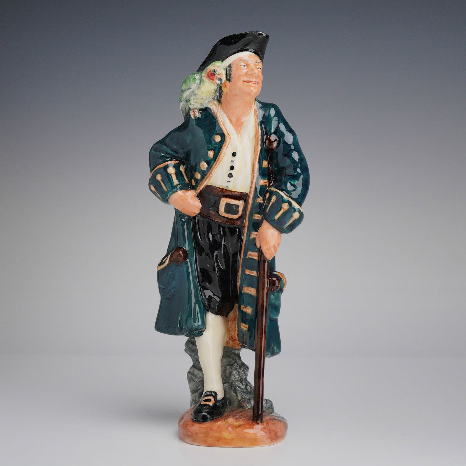 Royal Doulton Figurine Long John Silver HN2204: The figure depicts the fictional pirate from Robert Louis Stevenson's Treasure Island standing with a wooden crutch and a green parrot perched on his right shoulder. The character is dressed in an
