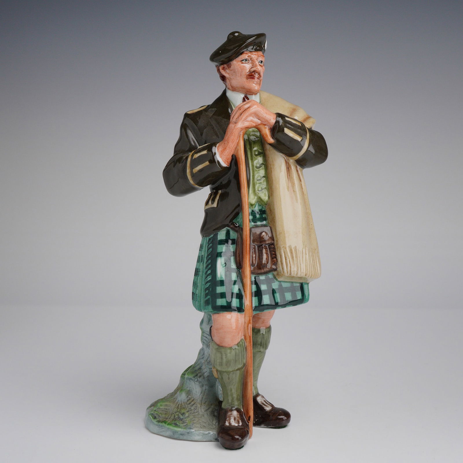 Royal Doulton Figurine The Laird HN2361: Designed by Mary Nicoll and issued circa 1967, the figure is depicted in traditional Scottish highland attire. The subject wears a dark brown jacket over a green waistcoat and a green and black