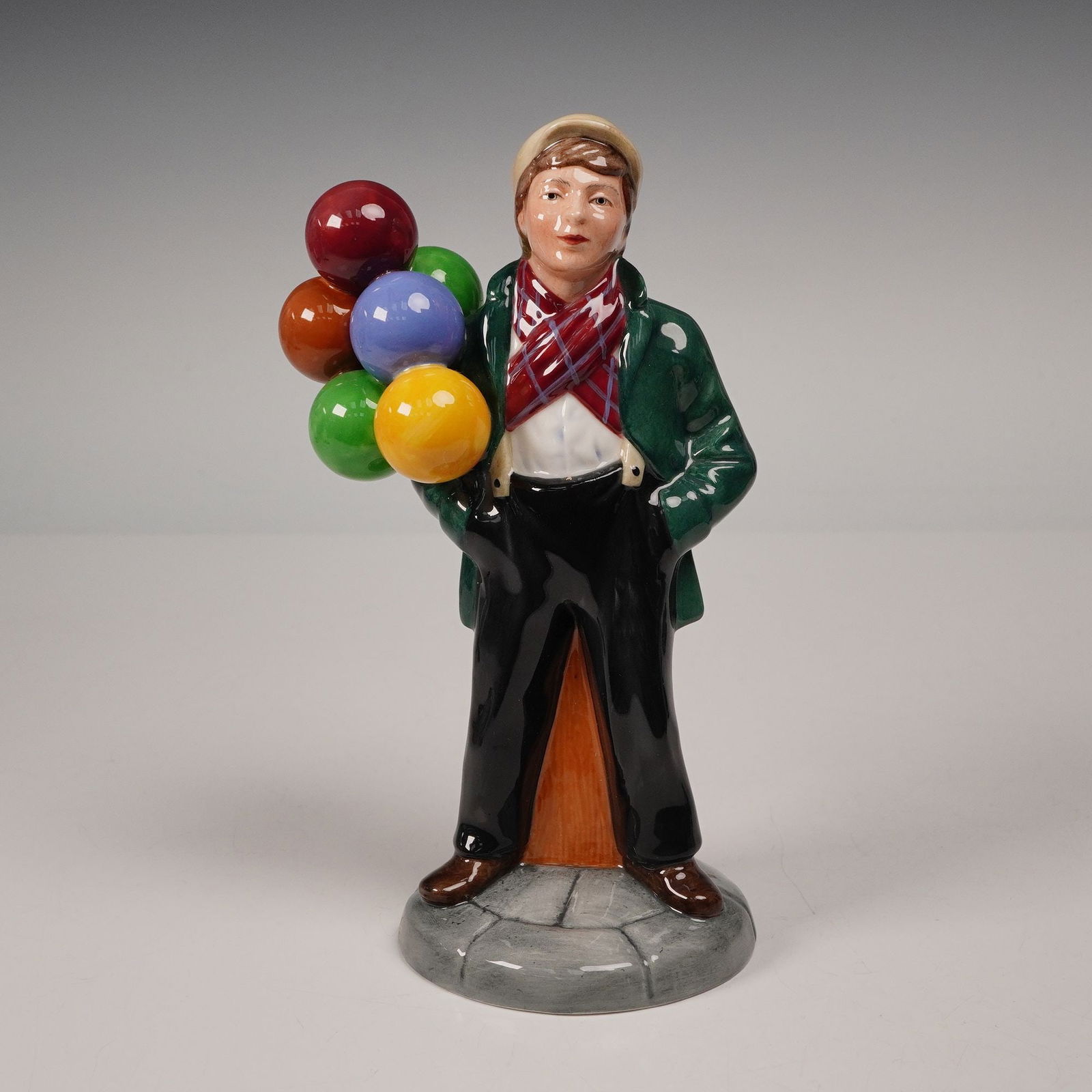 Royal Doulton Figurine, Balloon Boy HN2934: Delightful porcelain figurine titled Balloon Boy HN2934, modeled by Peter Gee and issued in 1983 as part of the Balloon Characters series. The figure depicts a young street vendor in a green