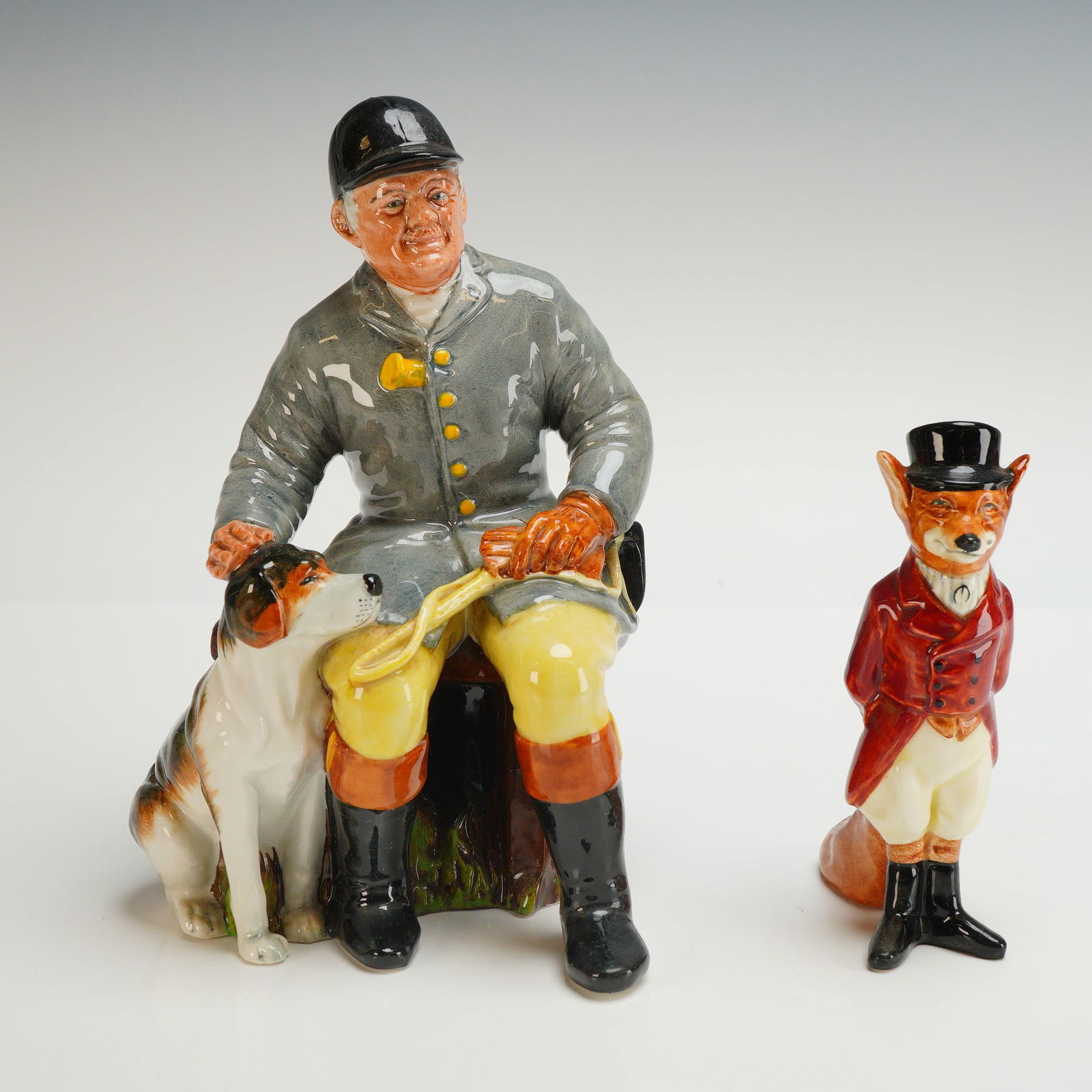 2pc Royal Doulton Figurines, The Huntsman HN2492 and Fox D6448: Two Royal Doulton figurines including The Huntsman HN2492 and Fox D6448. The larger figure, titled The Huntsman, depicts a seated man in traditional hunting attire featuring a grey coat, yellow breech