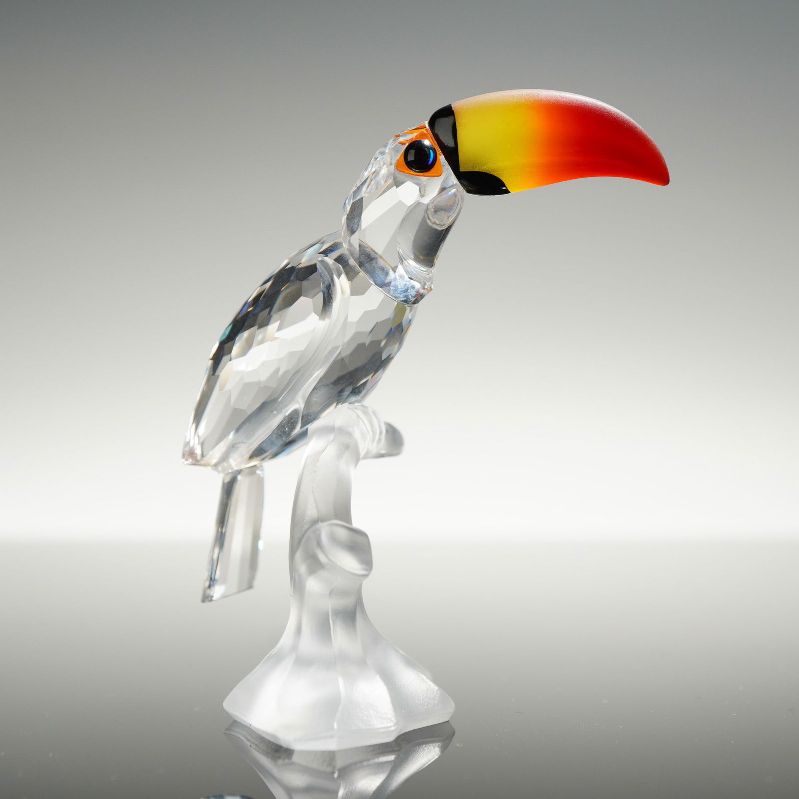 Swarovski Crystal Feathered Beauties Toucan Figurine: This Swarovski crystal figurine is part of the Feathered Beauties collection, identified by reference numbers 7621NR000006 and 234311. The piece features a faceted clear crystal body and tail perched