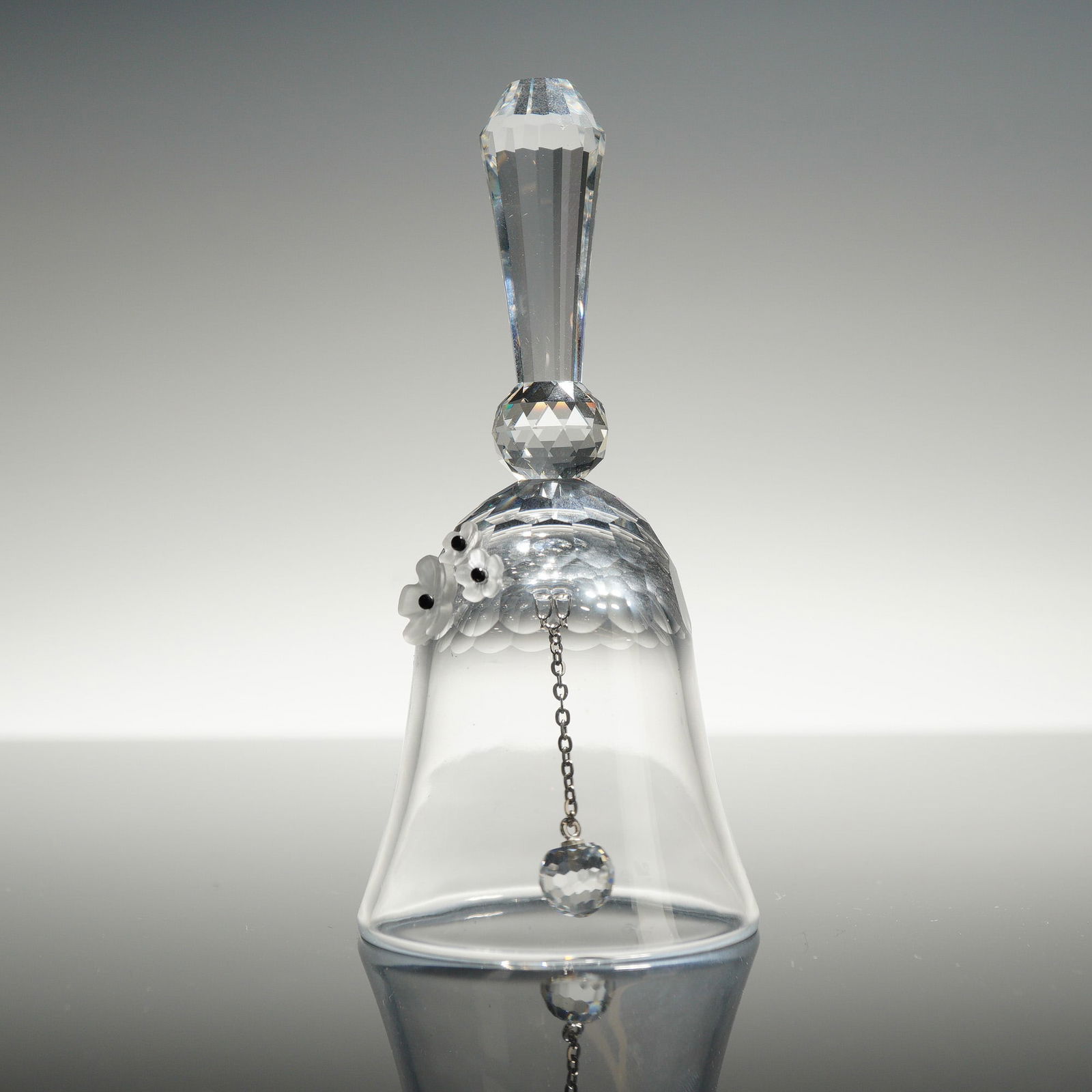 Swarovski Crystal Table Bell: A Swarovski Crystal Table Bell crafted from clear lead crystal. The piece features a tapered, multi-faceted handle joined to the bell body by a spherical faceted bead. The shoulder of the bell is deco