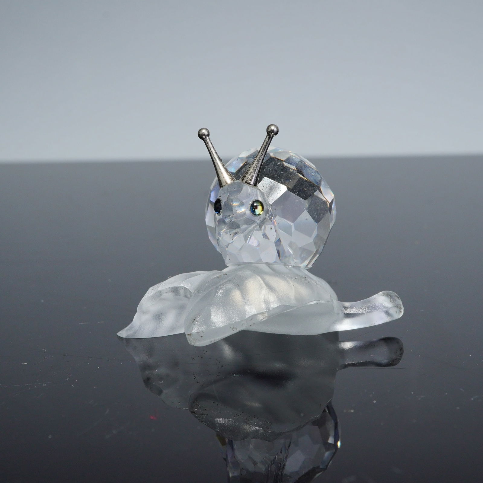 Swarovski Silver Crystal Figurine, Snail on a Vine Leaf: A Swarovski Silver Crystal figurine, model number 196501, identified as Snail on a Vine Leaf. The figurine is composed of a faceted clear crystal snail shell and body, featuring two small iridescent