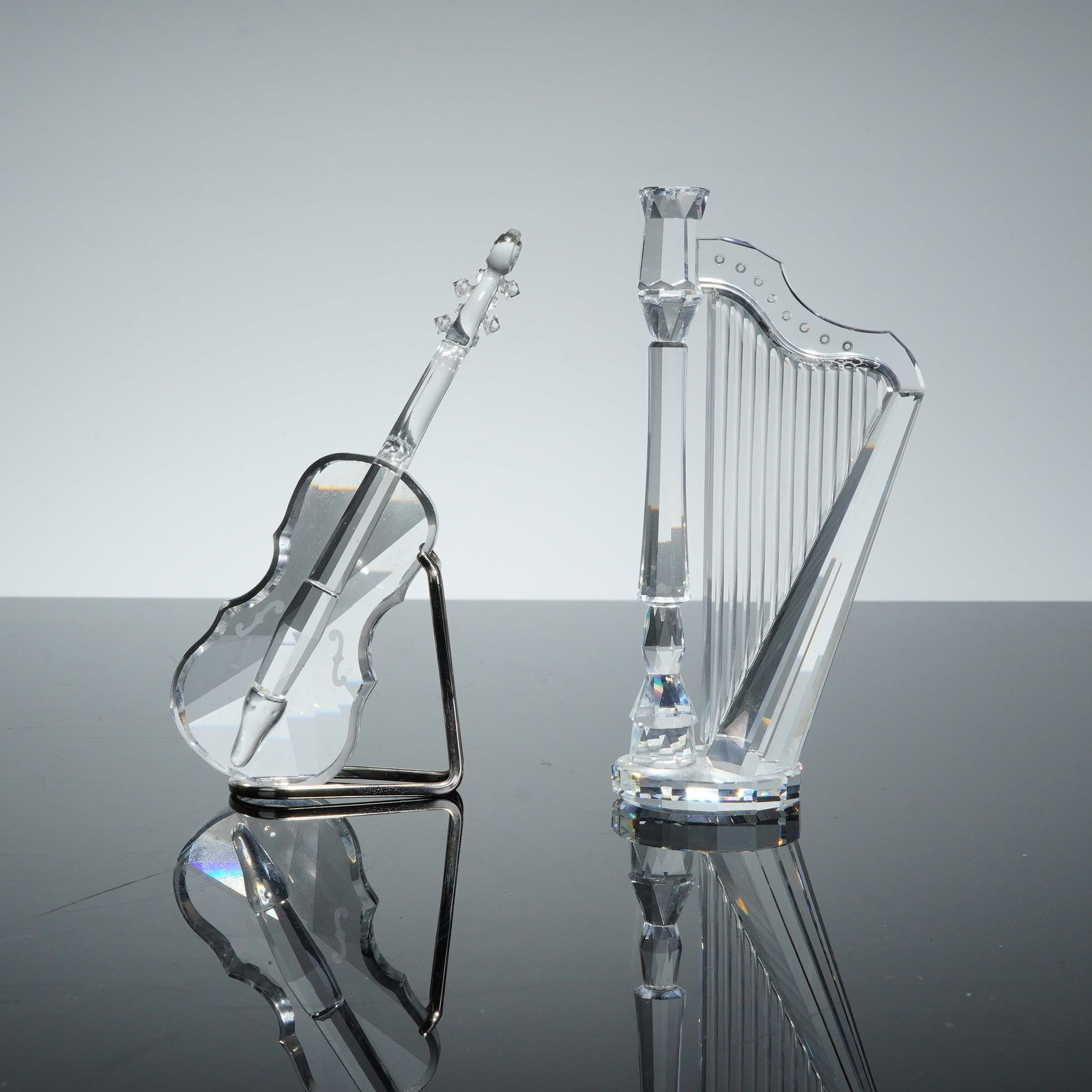 2pc Swarovski Silver Crystal Figurines, Harp and Violin: A pair of Swarovski Silver Crystal figurines from the musical instruments series, comprising a harp and a violin. Each piece is crafted from clear, multifaceted lead crystal. The harp features