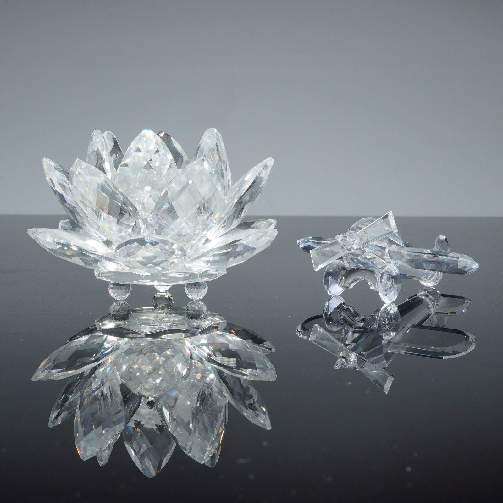 2pc Swarovski Silver Crystal Figurines, Waterlily Candleholder and Biplane: Two Swarovski Silver Crystal figurines including a Waterlily candleholder and a biplane. The Waterlily candleholder is designed with multiple tiers of pointed faceted petals and rests on three