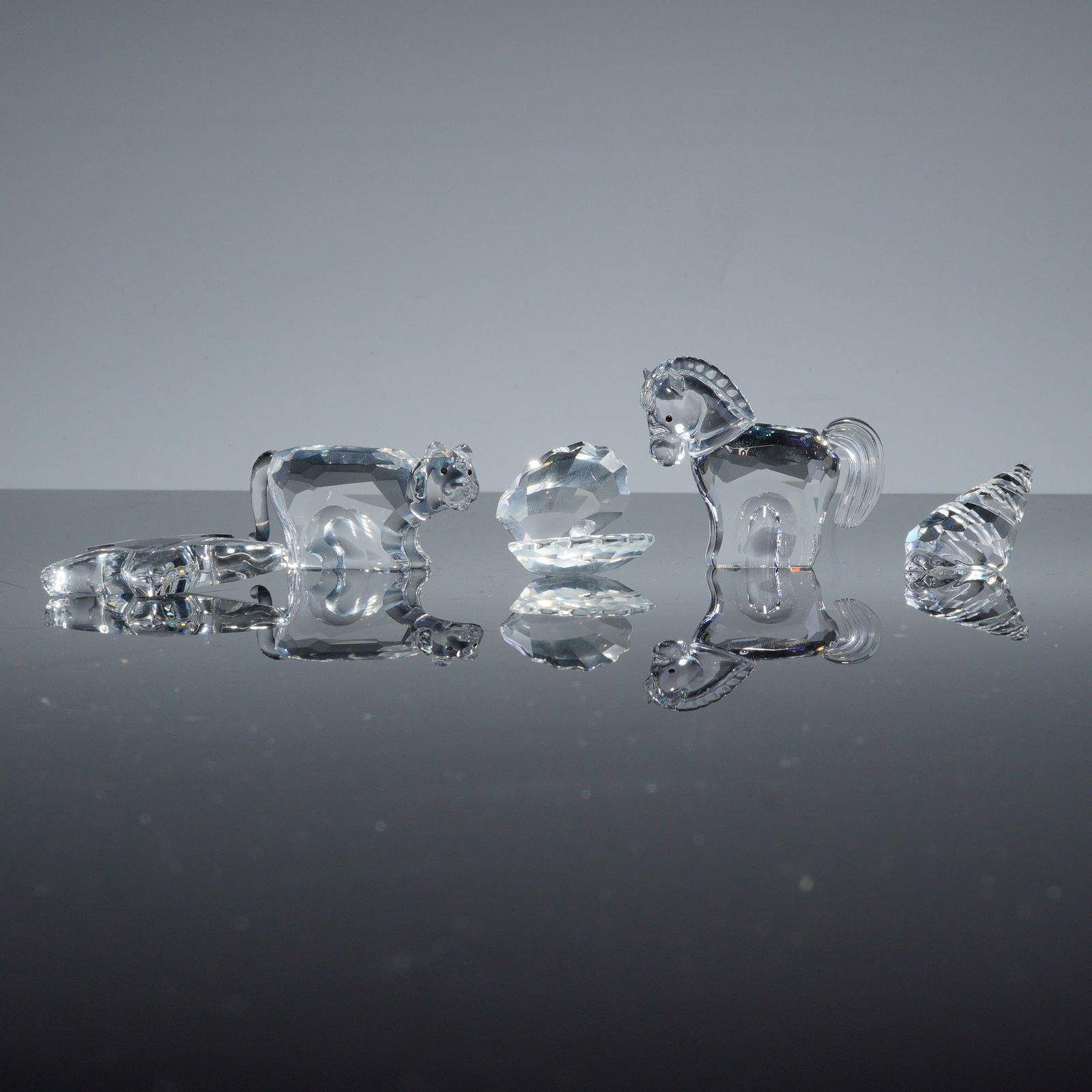 5pc Swarovski Crystal Figurines: A collection of contemporary faceted lead crystal figurines by Swarovski. The group includes a Chinese Zodiac Horse (model 289908), a tiger, an oyster with a pearl, and shells. Each piece is crafted f
