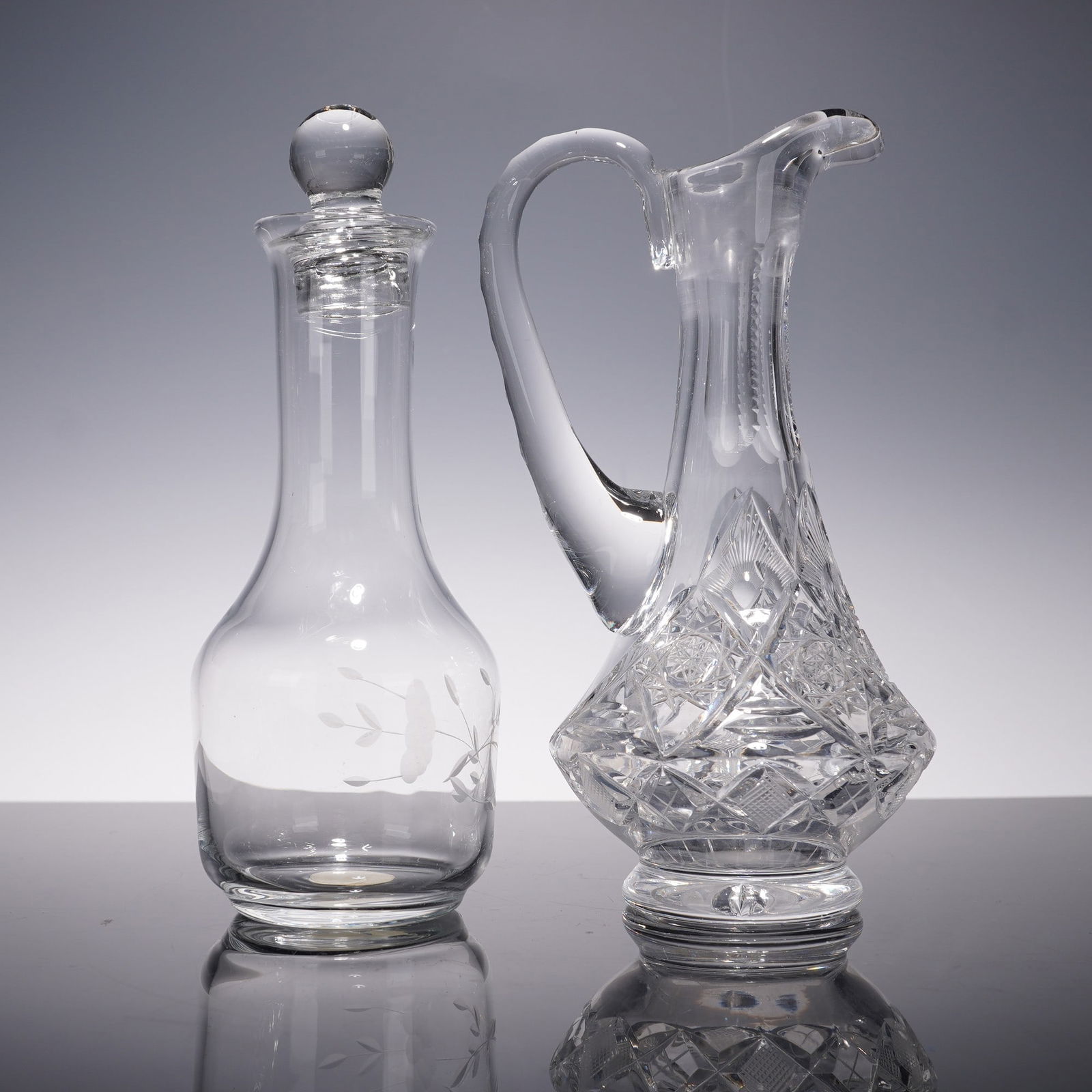 2pc Princess House Oil and Vinegar Crystal Cruets: Pair of elegant clear glass oil and vinegar cruets, including one etched glass cruet with a rounded stopper and frosted leaf motif, and one intricately cut crystal cruet with a faceted handle, wide ba