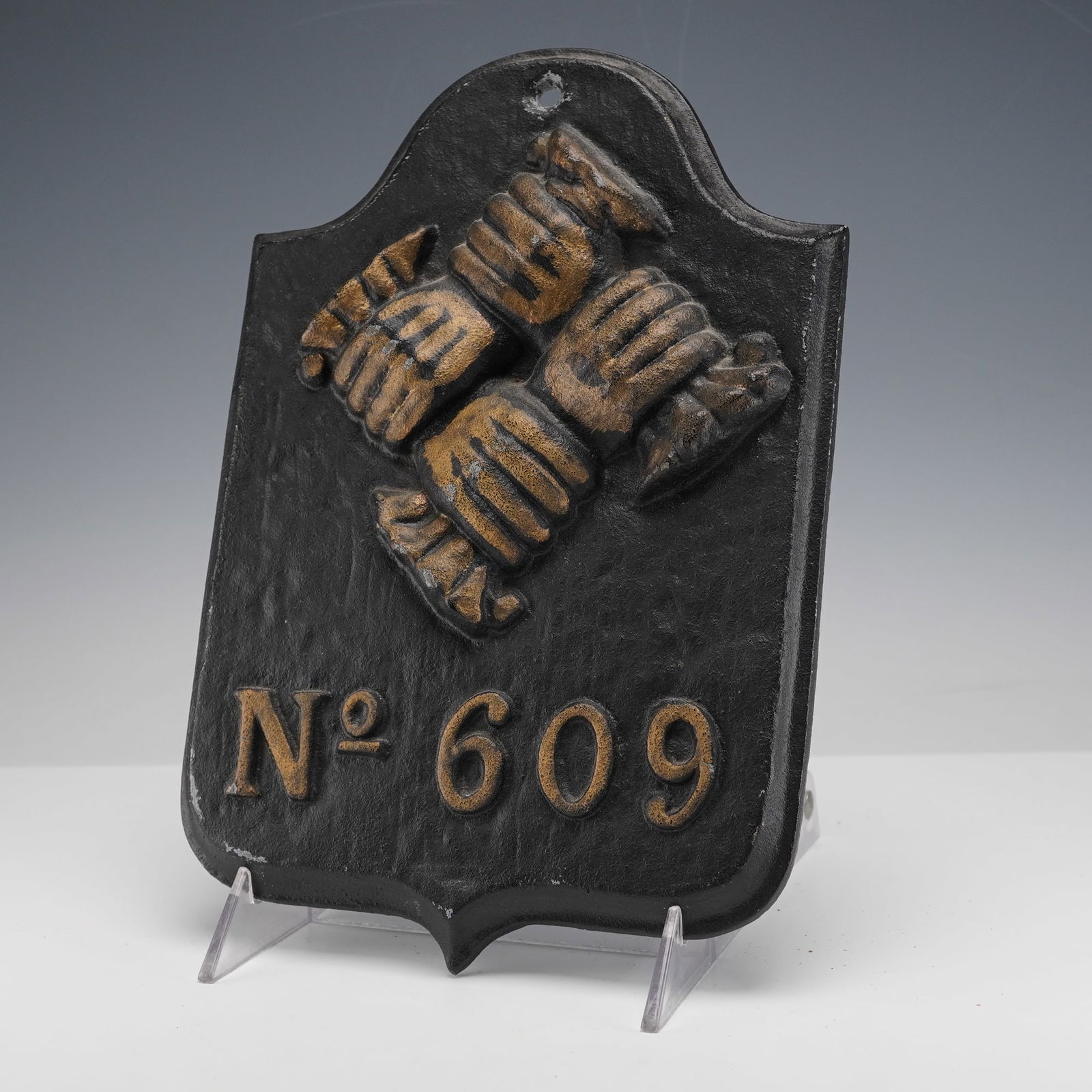 Cast Iron No 909 Fire Mark Plaque: Cast iron fire mark in shield form with a raised motif of four clasped hands arranged in a diamond above the cast designation No 909, the surface finished in black with worn bronze accents to the reli