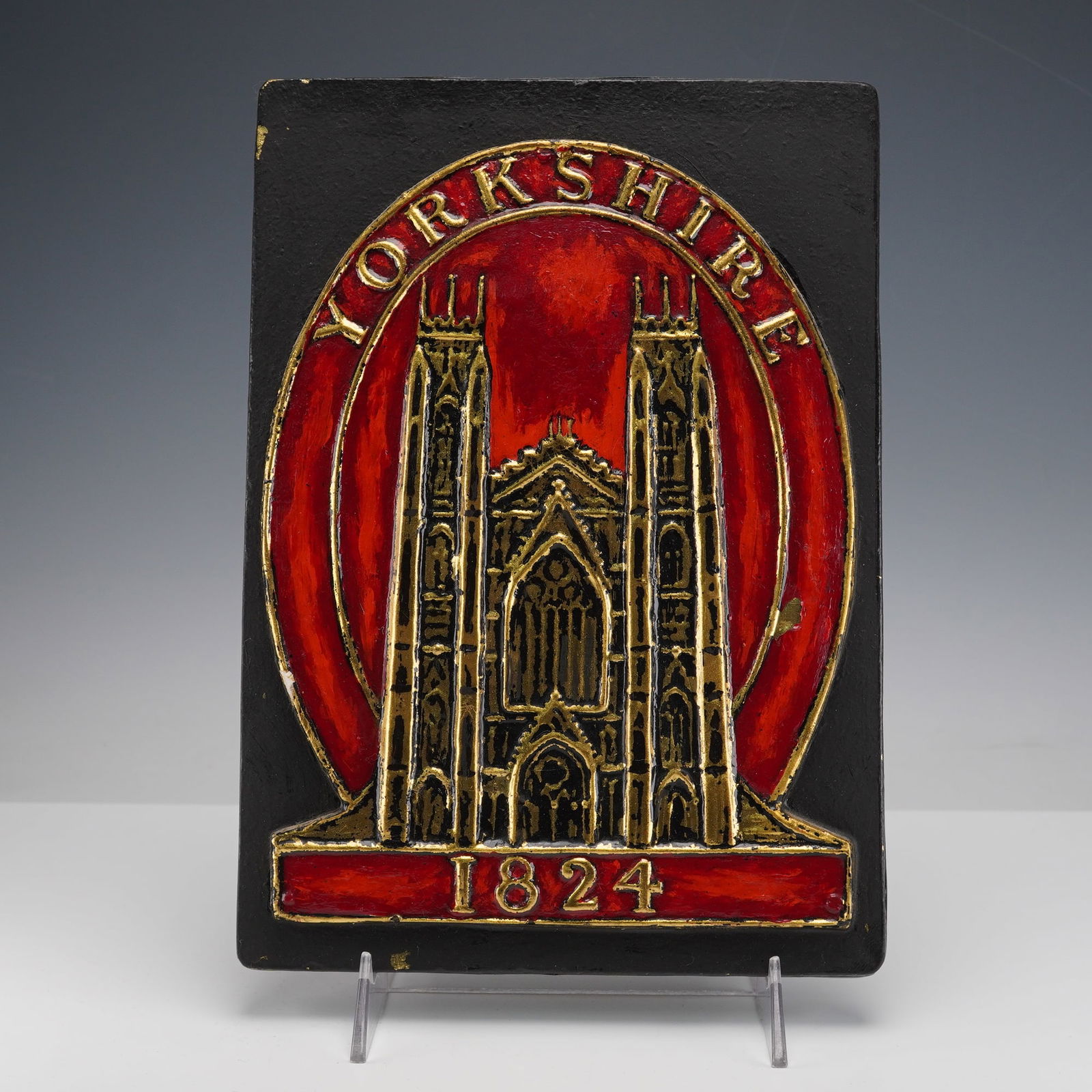 Yorkshire Assurance Company Fire Mark Plaque: his plaque shows a raised gold colored cathedral design against a bright red background with Yorkshire across the top and 1824 at the bottom. It is mounted on a black backing and has a label on the re