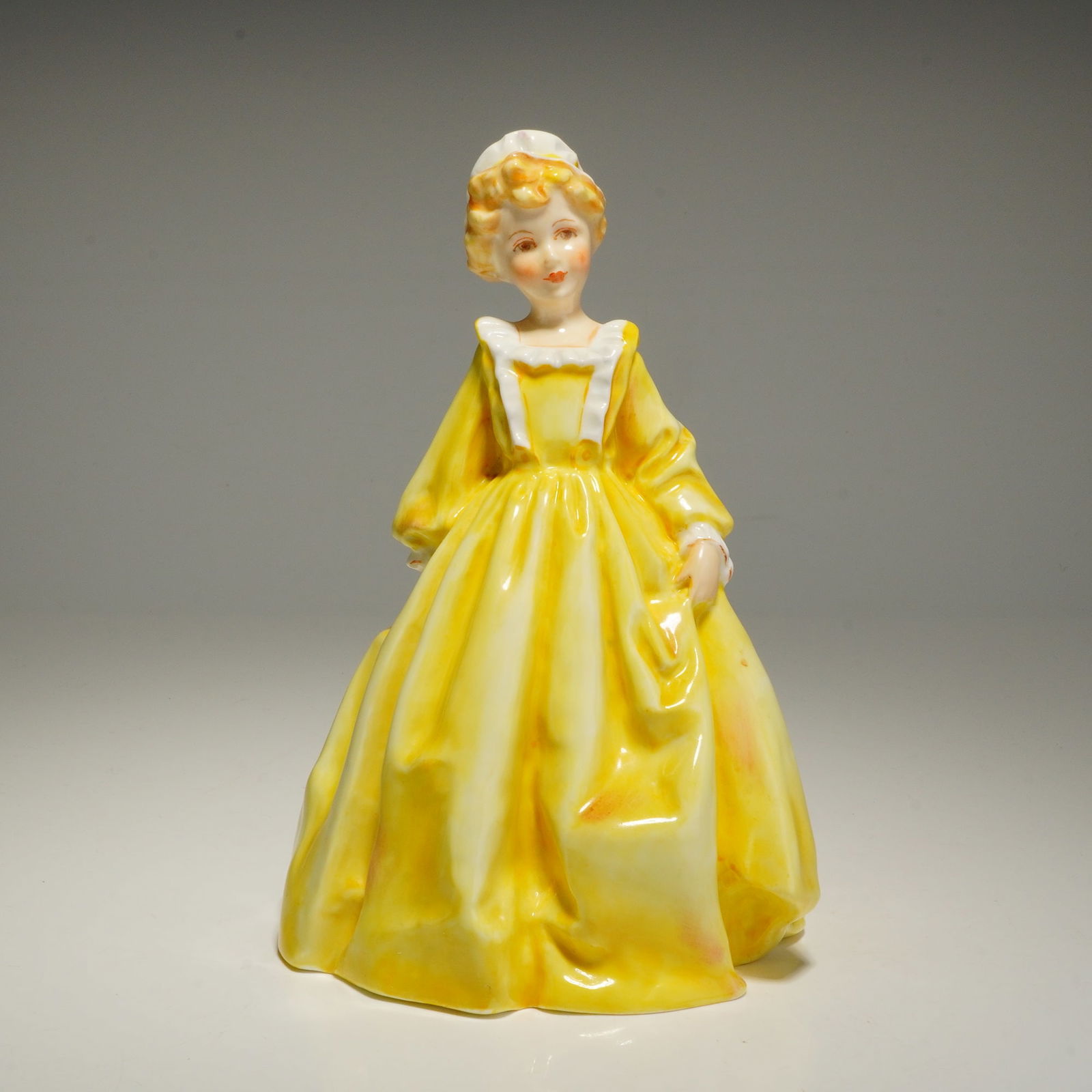 Royal Worcester Grandmother's Dress Figurine Model 3081: This Royal Worcester figurine titled Grandmother's Dress 3081 was designed by Freda Doughty. The bone china piece depicts a young woman in a voluminous yellow gown with long sleeves and a white ruffle