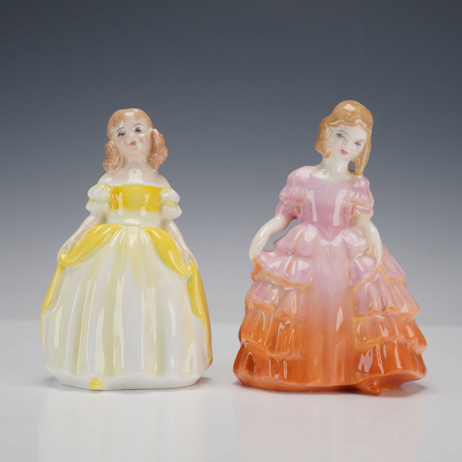 2pc Royal Doulton Figurines, Penny and Rose: Two hand-painted porcelain figures comprising Penny HN2424 and Rose HN1368. Penny is modeled wearing a yellow gown while Rose is depicted in graduated pink and orange ruffled dress; each modeled as a