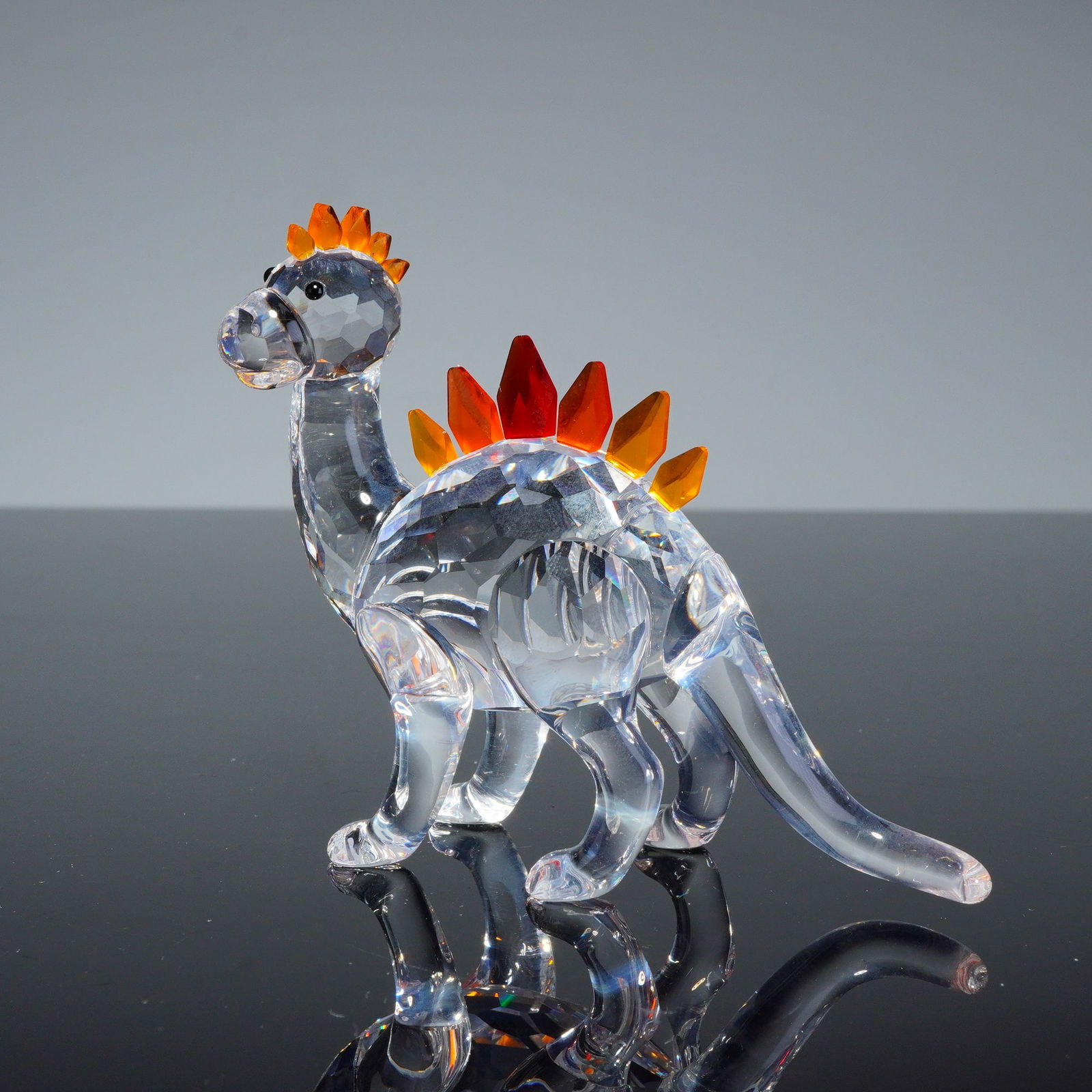 Swarovski Crystal Figurine, Dino the Dinosaur: A Swarovski crystal figurine titled Dino the Dinosaur, model number 268204. The piece is constructed from faceted clear crystal forming the body, neck, and head. The tail and legs are rendered in smoo