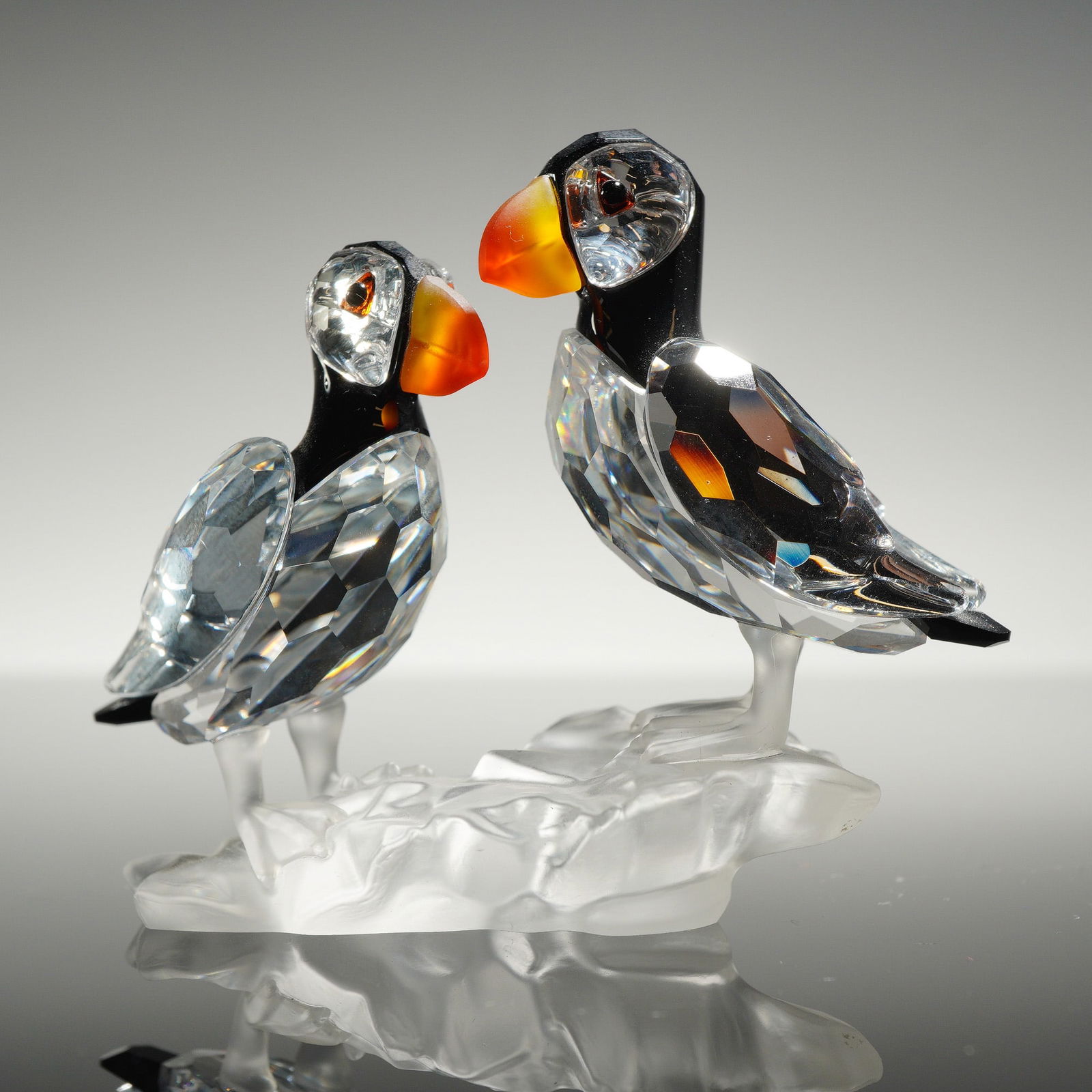 Swarovski Silver Crystal Puffins Figurine: A Swarovski Silver Crystal figurine, model number 261643, featuring a pair of puffins perched on a frosted, crag-like base. The birds are constructed from faceted clear crystal wings and lower bodies,