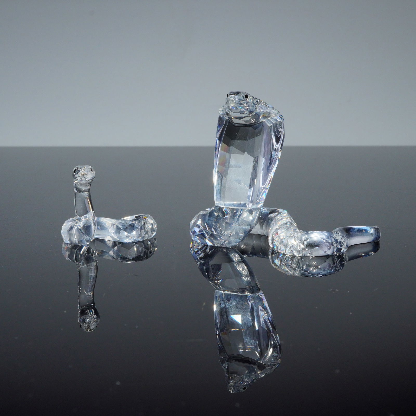 2pc Swarovski Crystal Figurines, Snakes: A pair of Swarovski Silver Crystal figurines depicting a cobra and a snake. Both items are constructed from clear, multifaceted lead crystal with sharp, geometric facets designed to reflect light. The