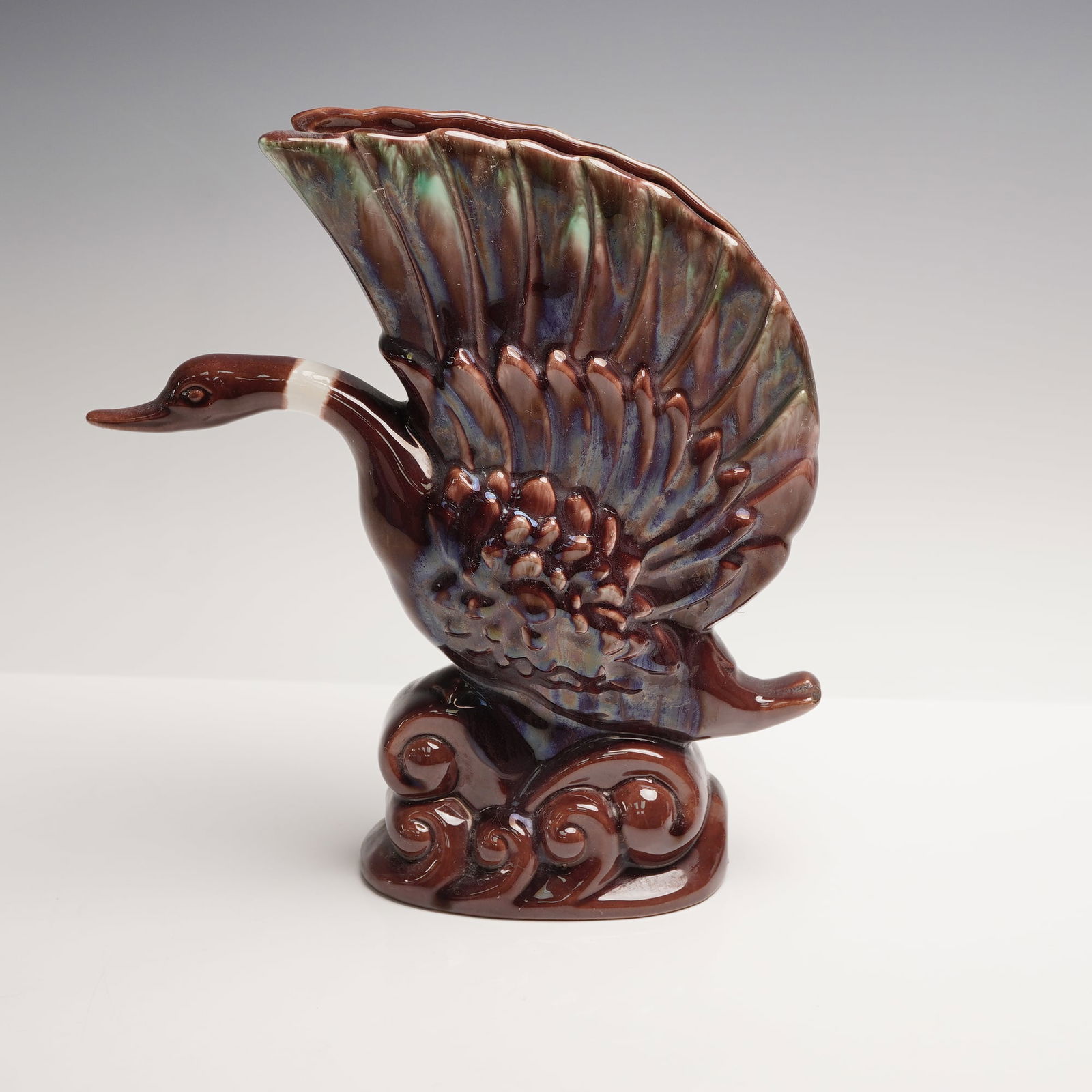 Royal Haeger Ceramic Goose Vase: A sculptural mid century, ceramic vessel rendered in high relief form, exhibiting an elegant avian figure with dramatically arched wings and stylized wave-form base. Finished in a multicolor mottled g