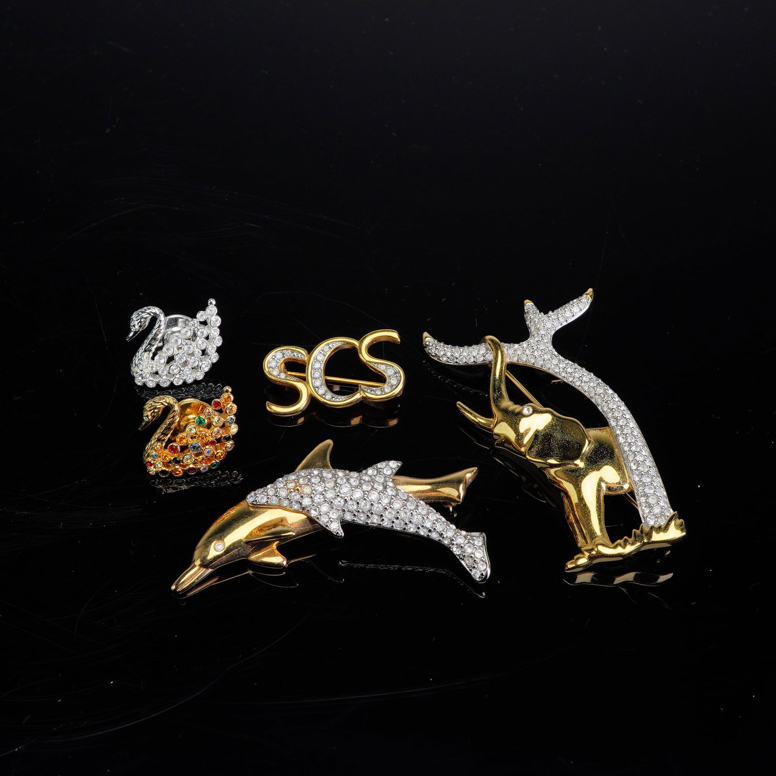 5pc Swarovski Crystal Brooch and Pin Collection: Collection features a variety of designs including jumping dolphins, an elephant, the SCS logo, and two swans. The items are crafted from polished gold-tone and silver-tone metals accented with