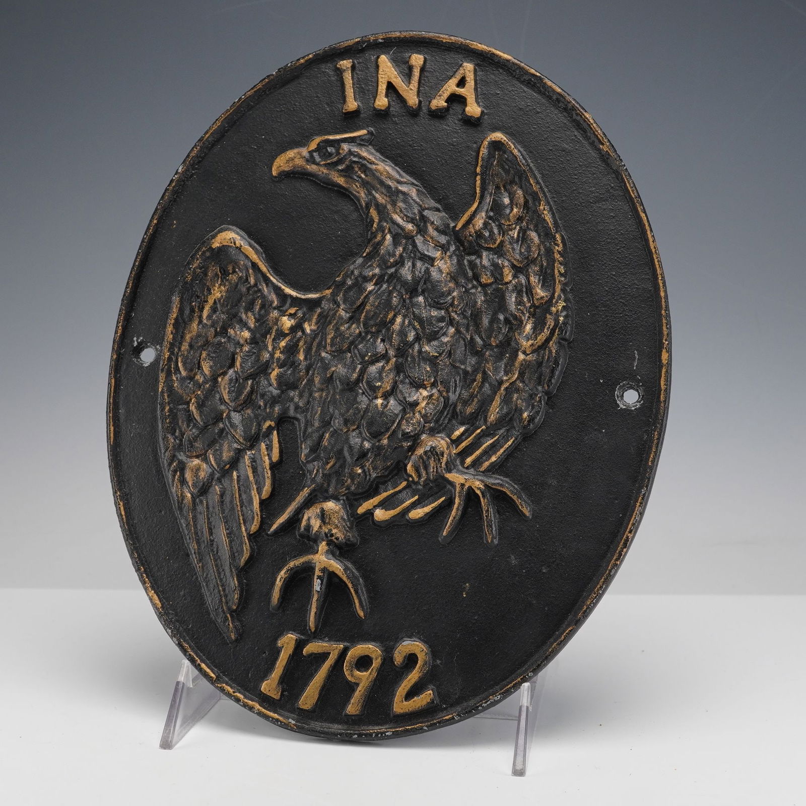 Cast Iron Fire INA Insurance Mark Plaque: This oval cast iron fire mark features a raised eagle with detailed feathering and outstretched wings, set against a matte black ground with gilt highlights that accentuate the lettering INA at the