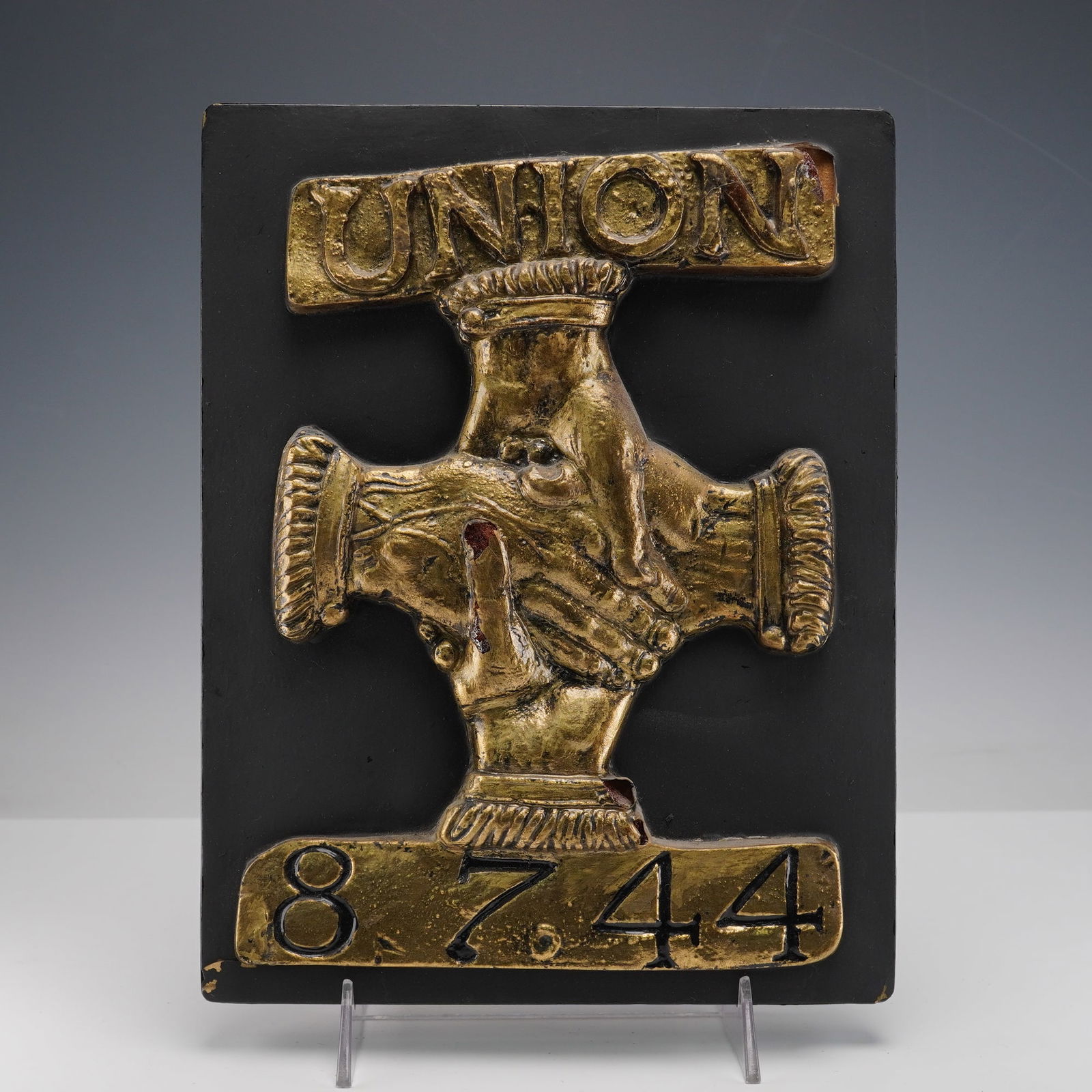 Union Assurance Society by E. V. Jackson Reproduction Fire Mark Plaque: his plaque features a raised gold colored design showing four clasped hands forming a cross, with Union in gold colored lettering above and the number 8744 below. It is mounted on a black backing,