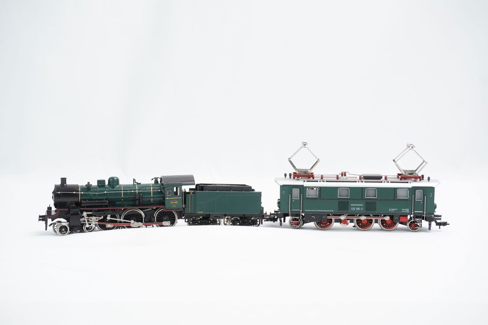 A Trio of HO Scale Model Locomotives, possibly Fleischmann or Marklin: A collection of three HO scale model railway components, comprising a steam locomotive engine, its associated tender, and a four-axle electric locomotive. The models are finished in a dark green and b